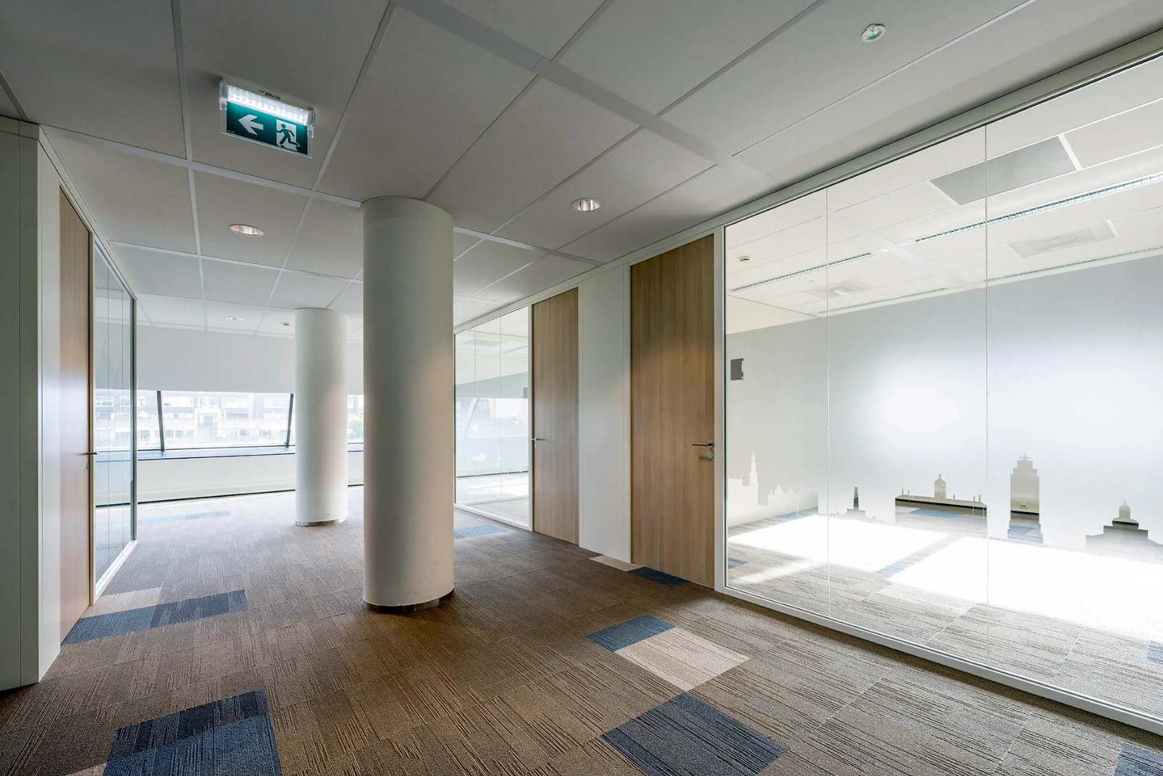 Modern office hallway at Rietlandpark with glass walls, wooden doors, and carpeted flooring.