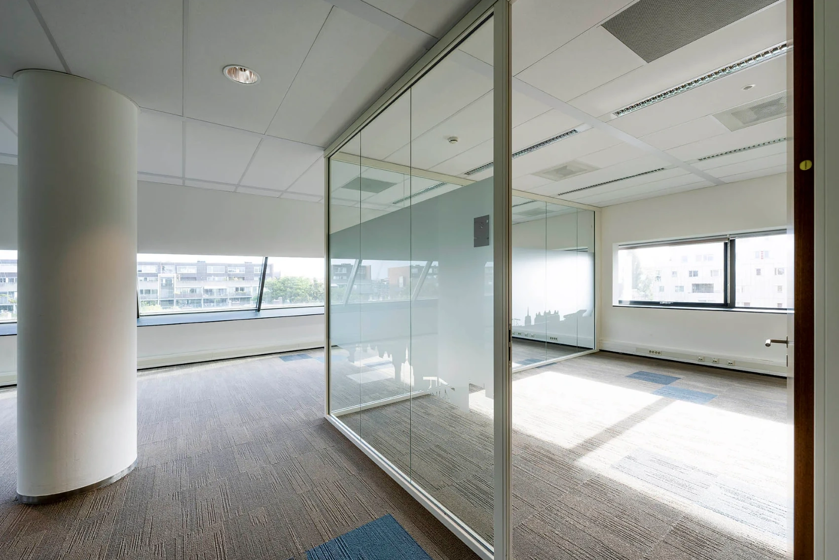 Modern office space at Rietlandpark with large windows, glass walls, and carpeted flooring.