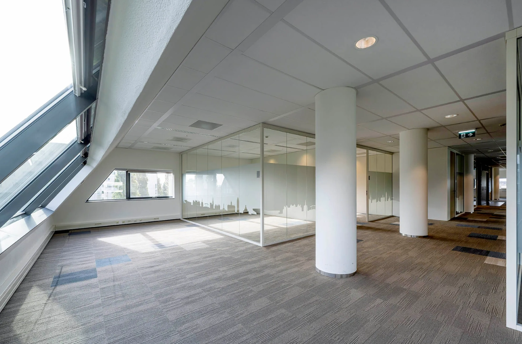 Modern office interior at Rietlandpark with slanted windows, glass meeting rooms, and carpeted floors.