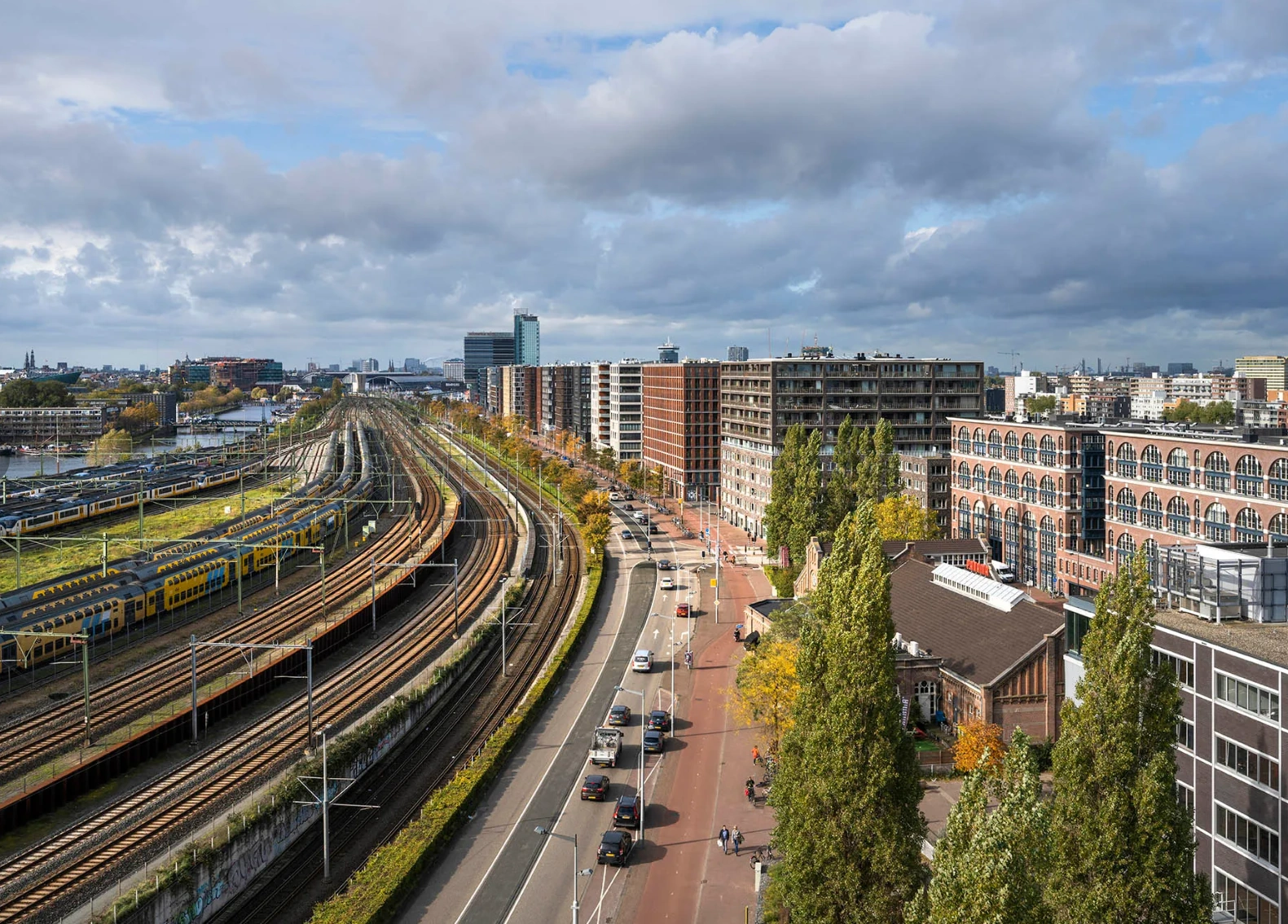Aerial view of Rietlandpark in Amsterdam, showing train tracks, residential buildings, and a busy street with cars and cyclists.