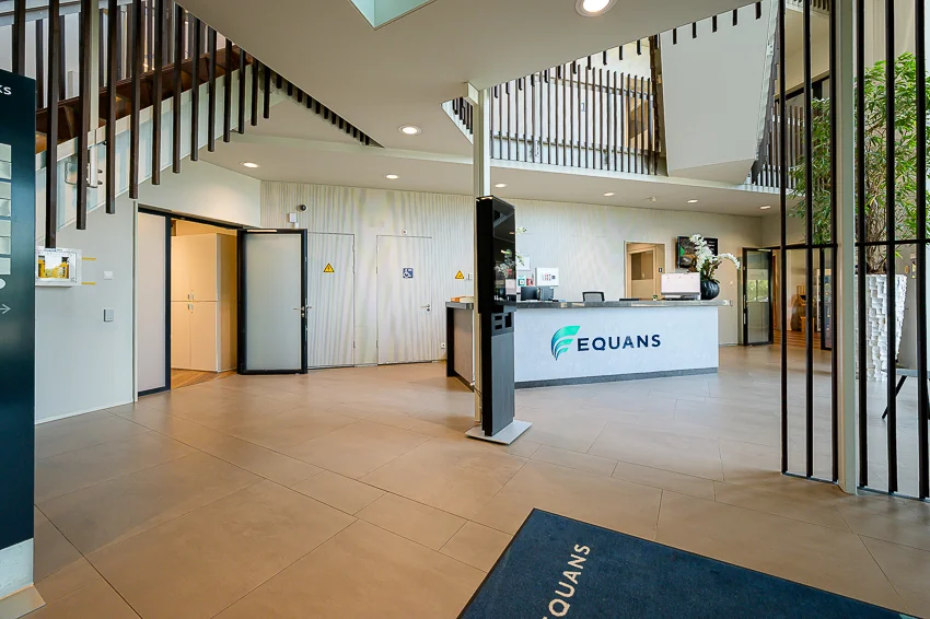 Modern reception area of Equans at Laan van Barcelona with a front desk, seating area, and staircase.