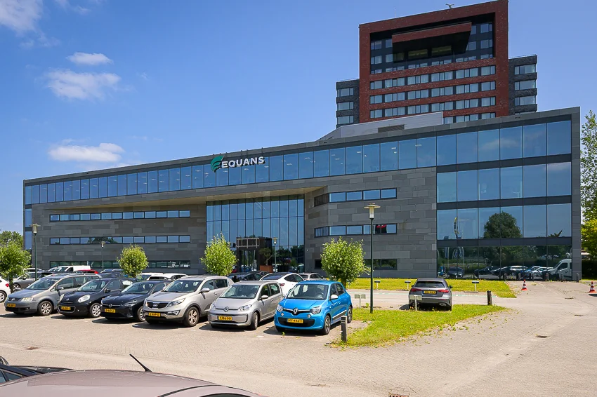Modern office building of EQUANS on Laan van Barcelona with parked cars in front.