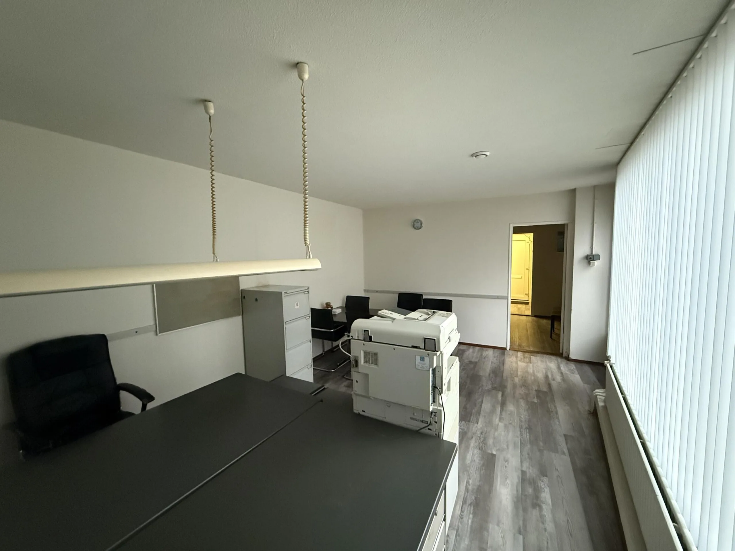 Office space on Katendrechtse Lagedijk with desks, chairs, a printer, and vertical blinds.