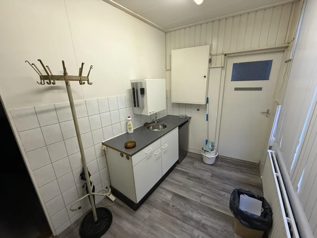 Small kitchenette at Katendrechtse Lagedijk with a sink, countertop, cleaning supplies, and a coat rack.