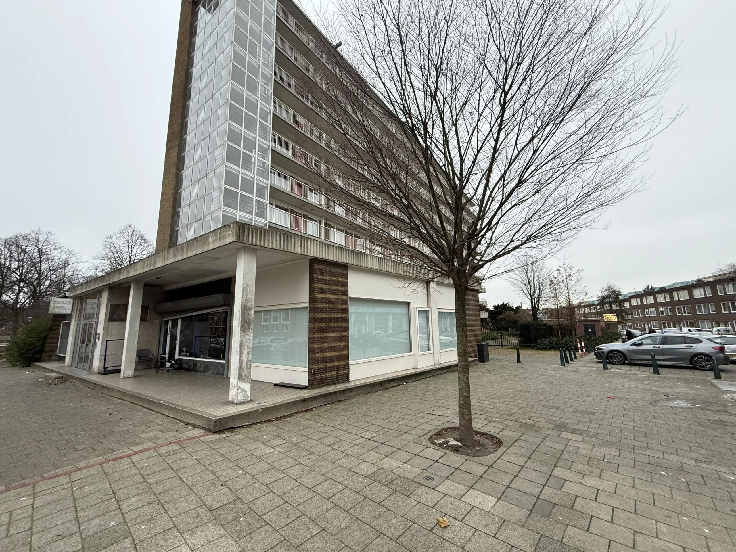 A street view of a residential apartment building on Katendrechtse Lagedijk with bare trees and parked cars on a cloudy day.