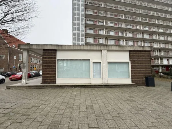 A small, modernist building on Katendrechtse Lagedijk with large windows and a high-rise apartment block in the background.