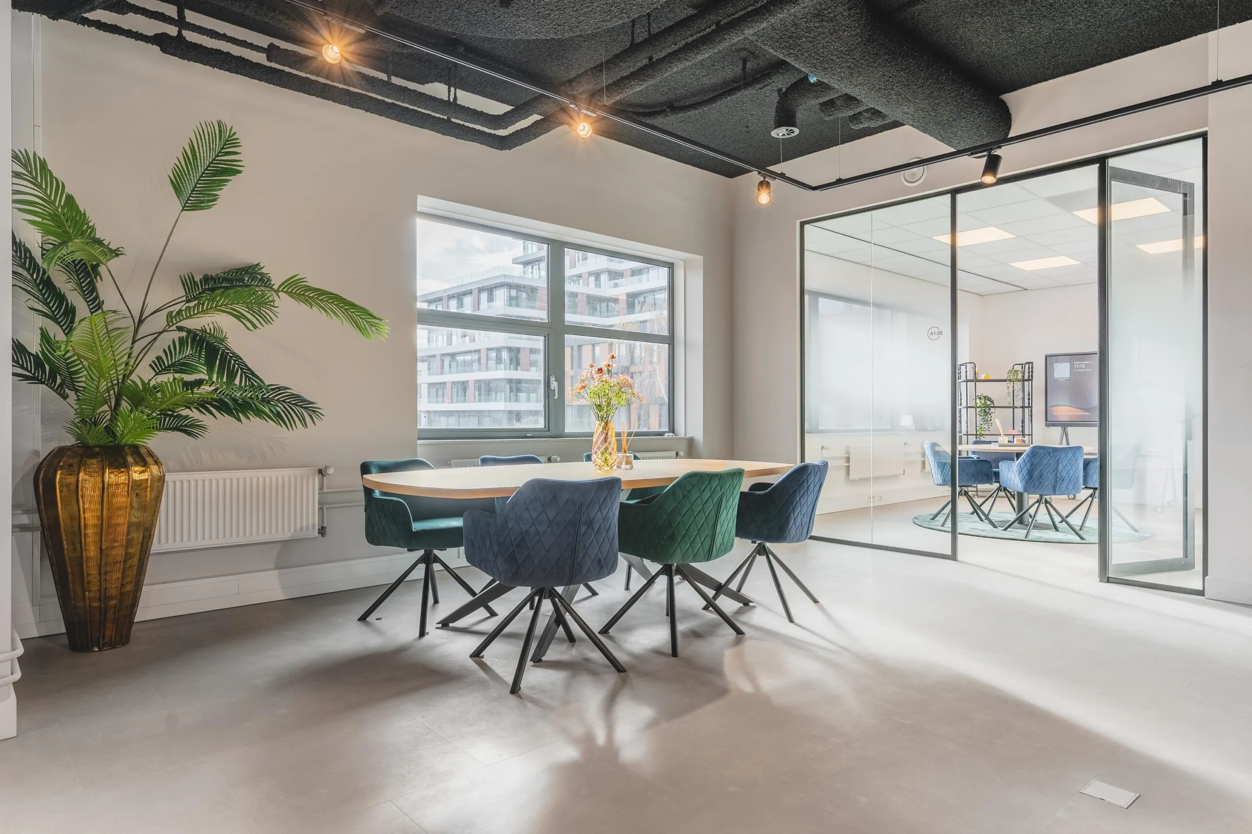 Modern meeting room on Paasheuvelweg with colorful velvet chairs, a large wooden table, and glass-walled office space.