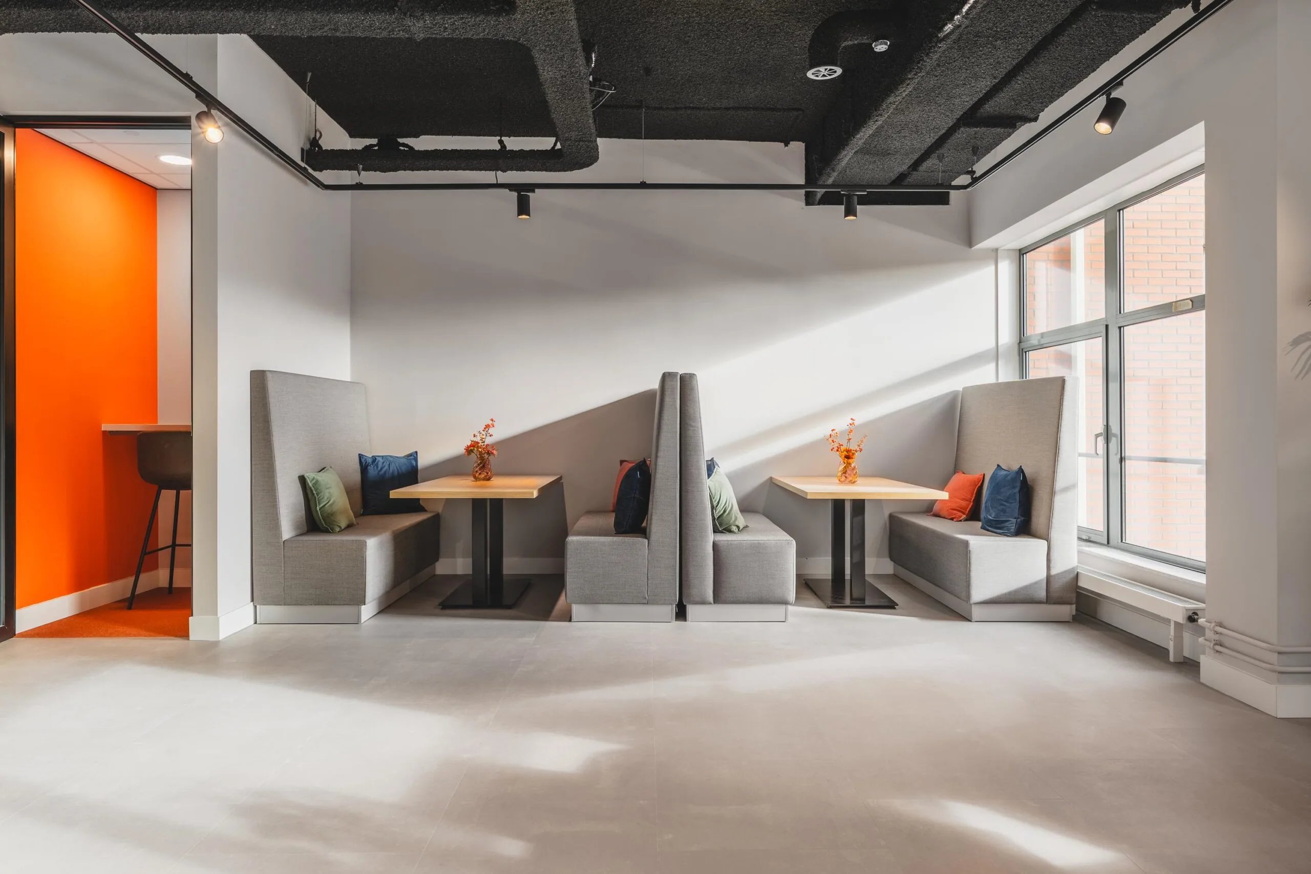 Modern seating area with high-back gray booths, colorful cushions, and wooden tables at Paasheuvelweg.