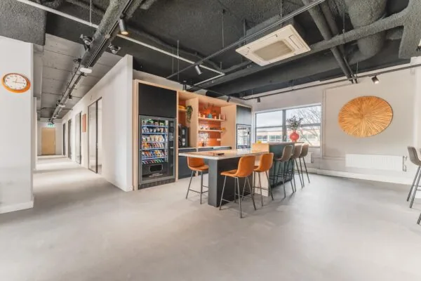 Modern office break area on Paasheuvelweg with vending machines, a high table with bar stools, and contemporary decor.