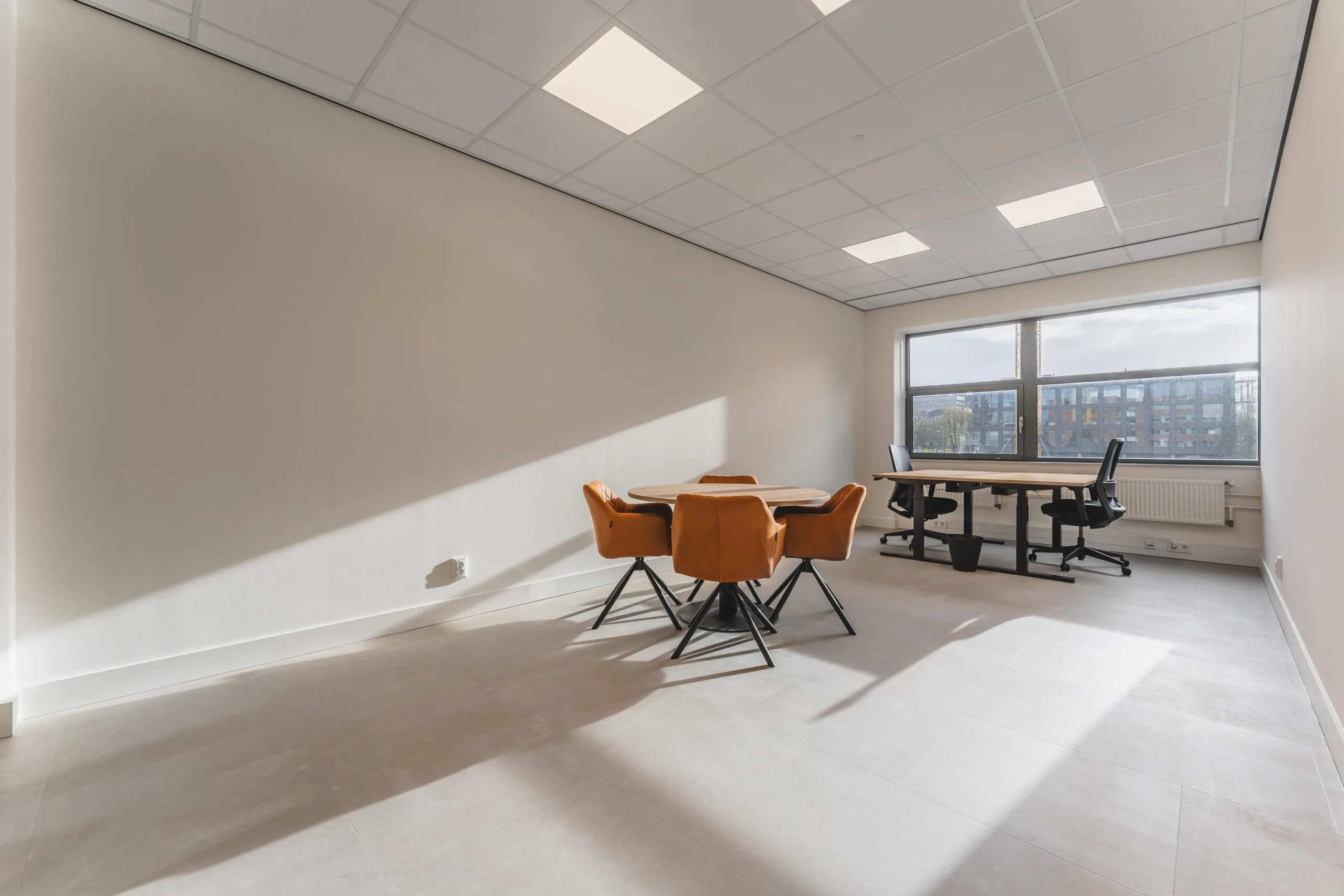 Modern office space on Paasheuvelweg with a meeting table, orange chairs, and large window with natural light.