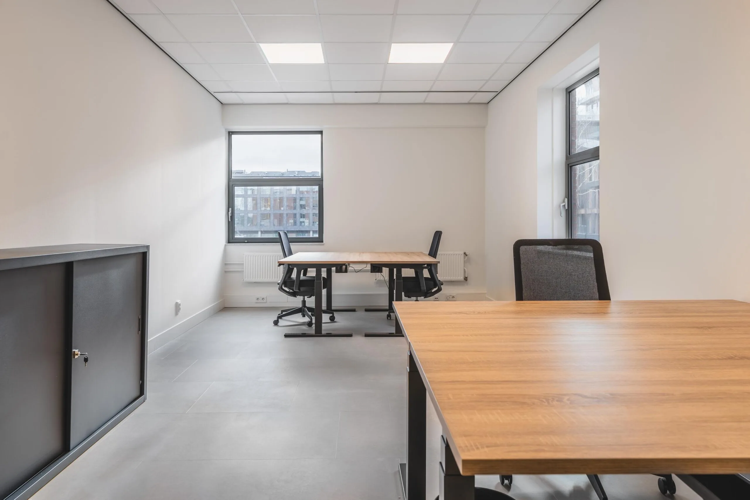 Modern office space on Paasheuvelweg with wooden desks, office chairs, and large windows providing natural light.