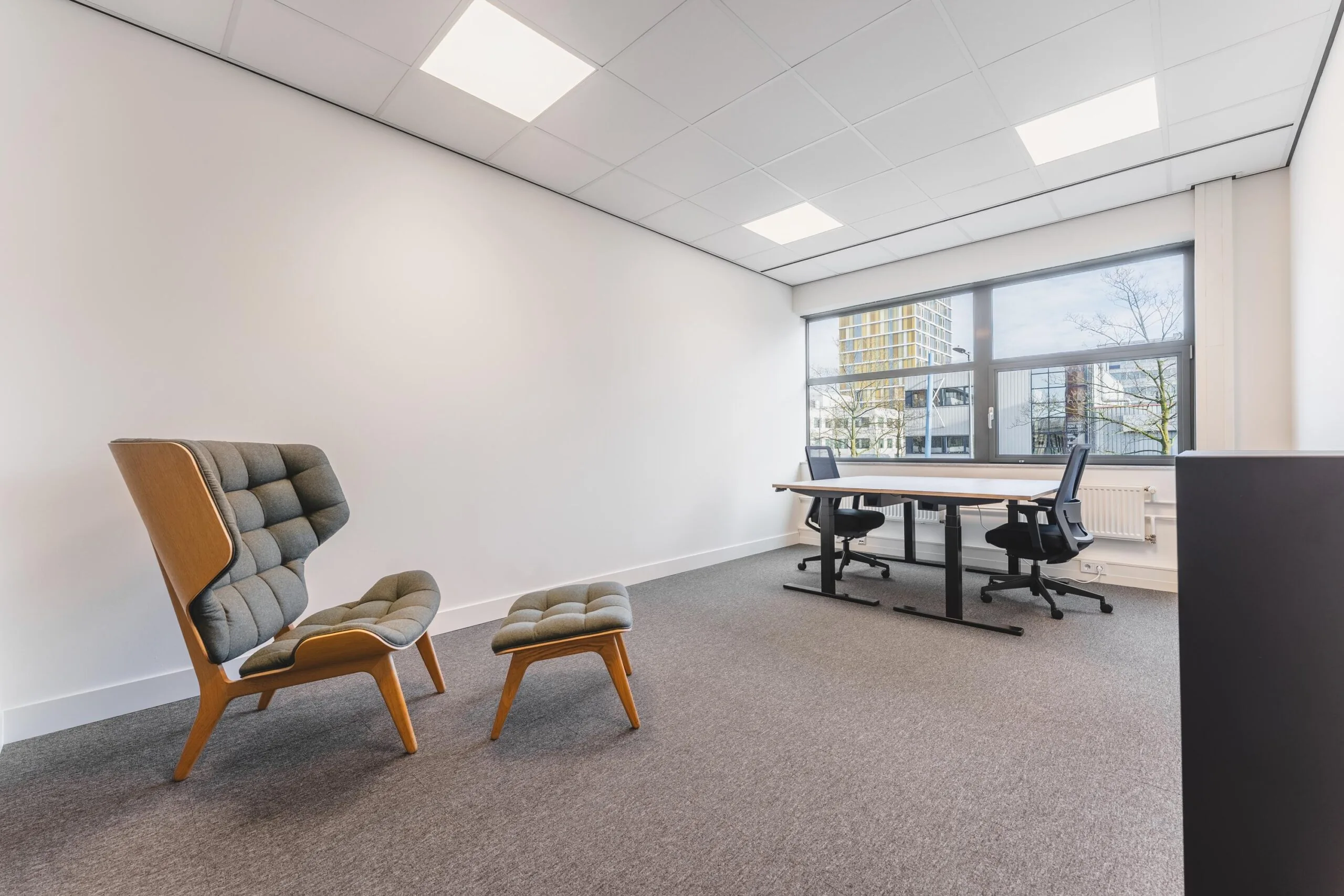 Modern office space at Paasheuvelweg with two desks, ergonomic chairs, and a lounge seating area by a large window.