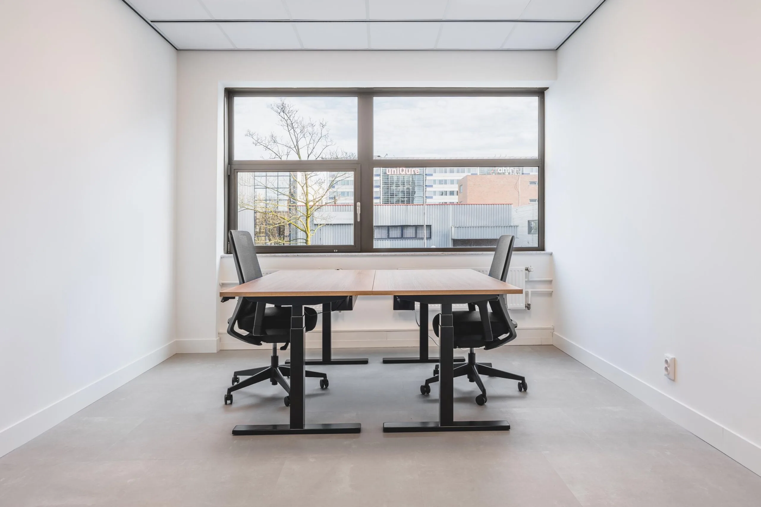 Modern, minimalistic office space on Paasheuvelweg with two desks and chairs by a large window.