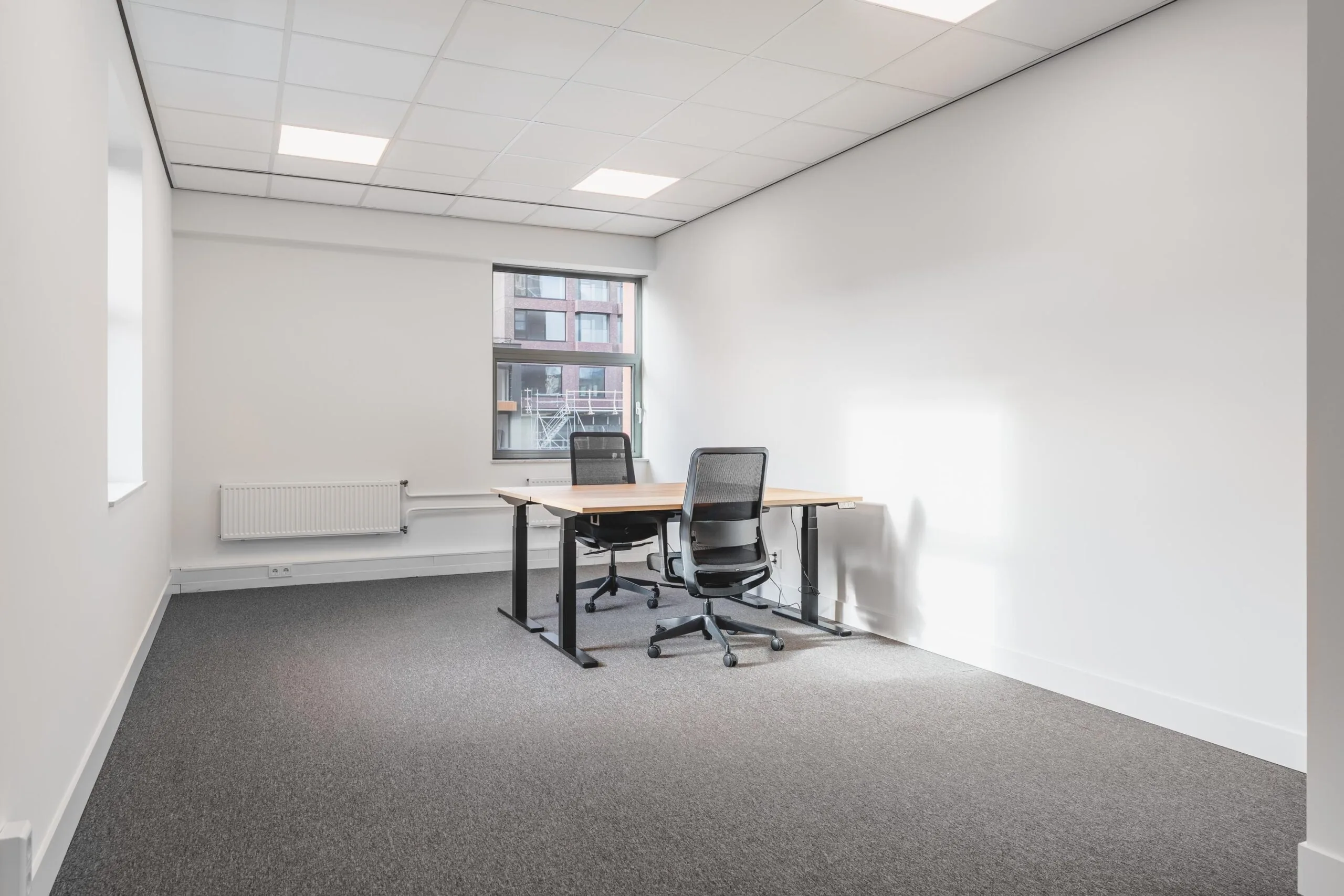 Minimalist office space at Paasheuvelweg with two chairs and a shared desk near a window.
