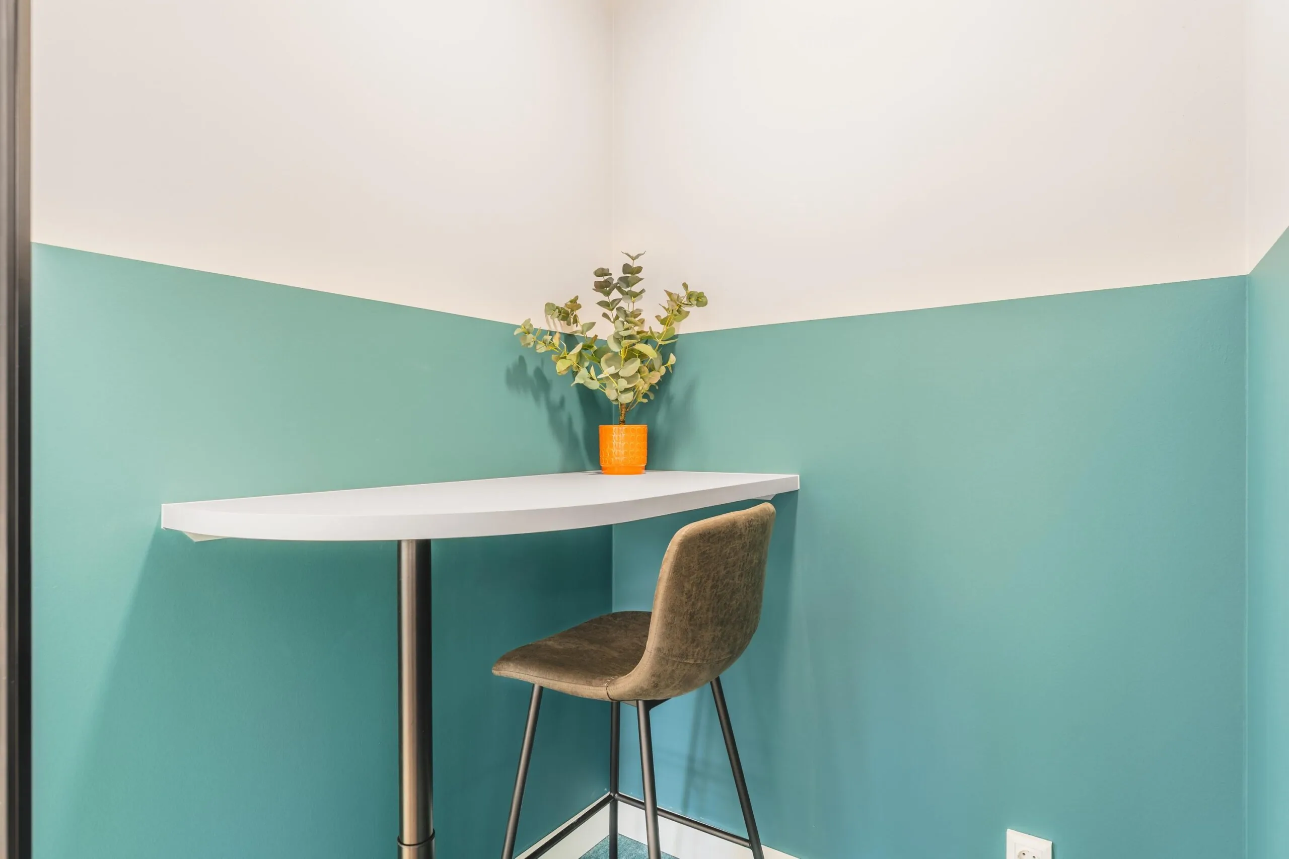 A small corner workspace with a high table, a bar stool, and a plant in an orange pot on Paasheuvelweg.