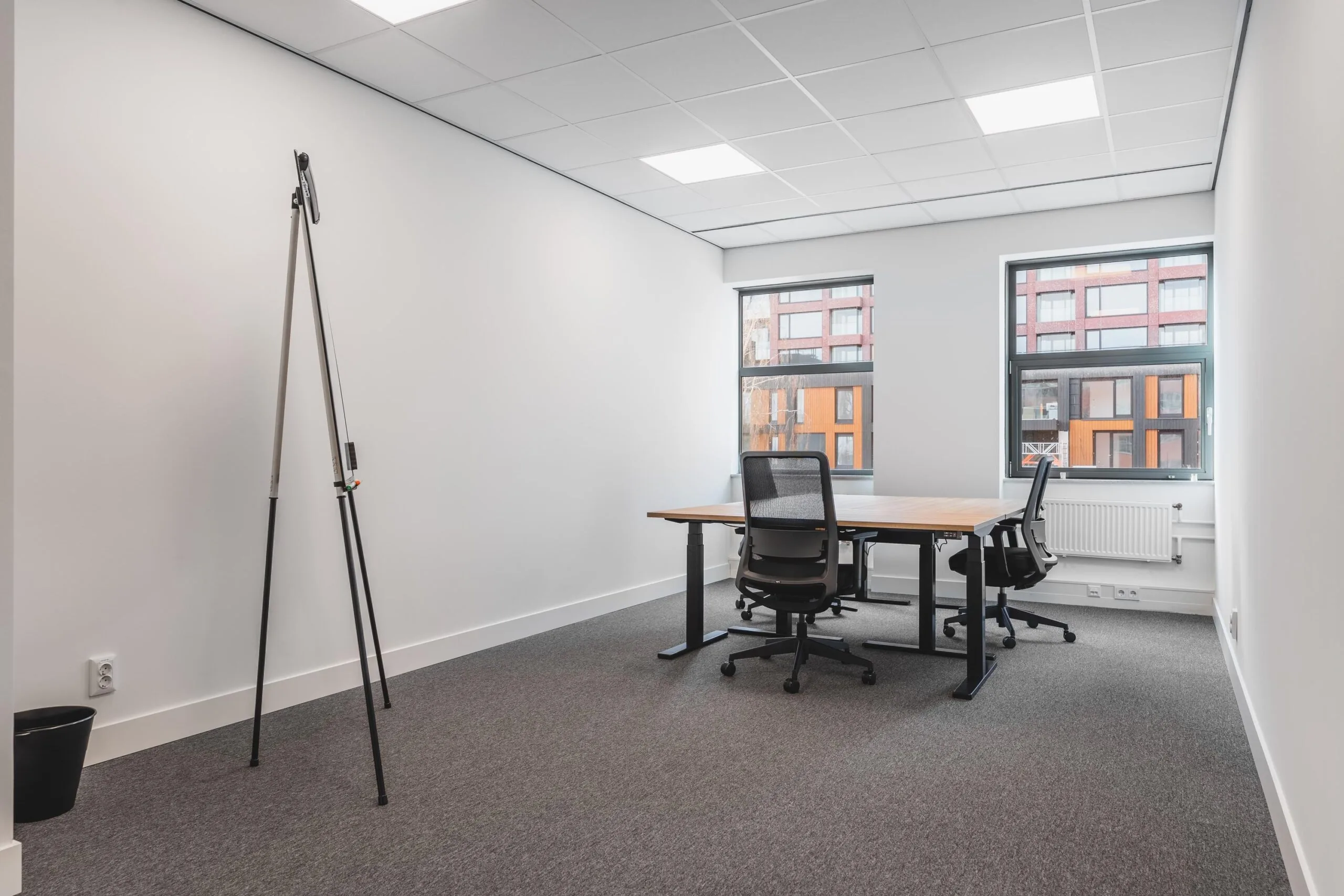 Modern, minimalistic office space at Paasheuvelweg with two desks, ergonomic chairs, and large windows.