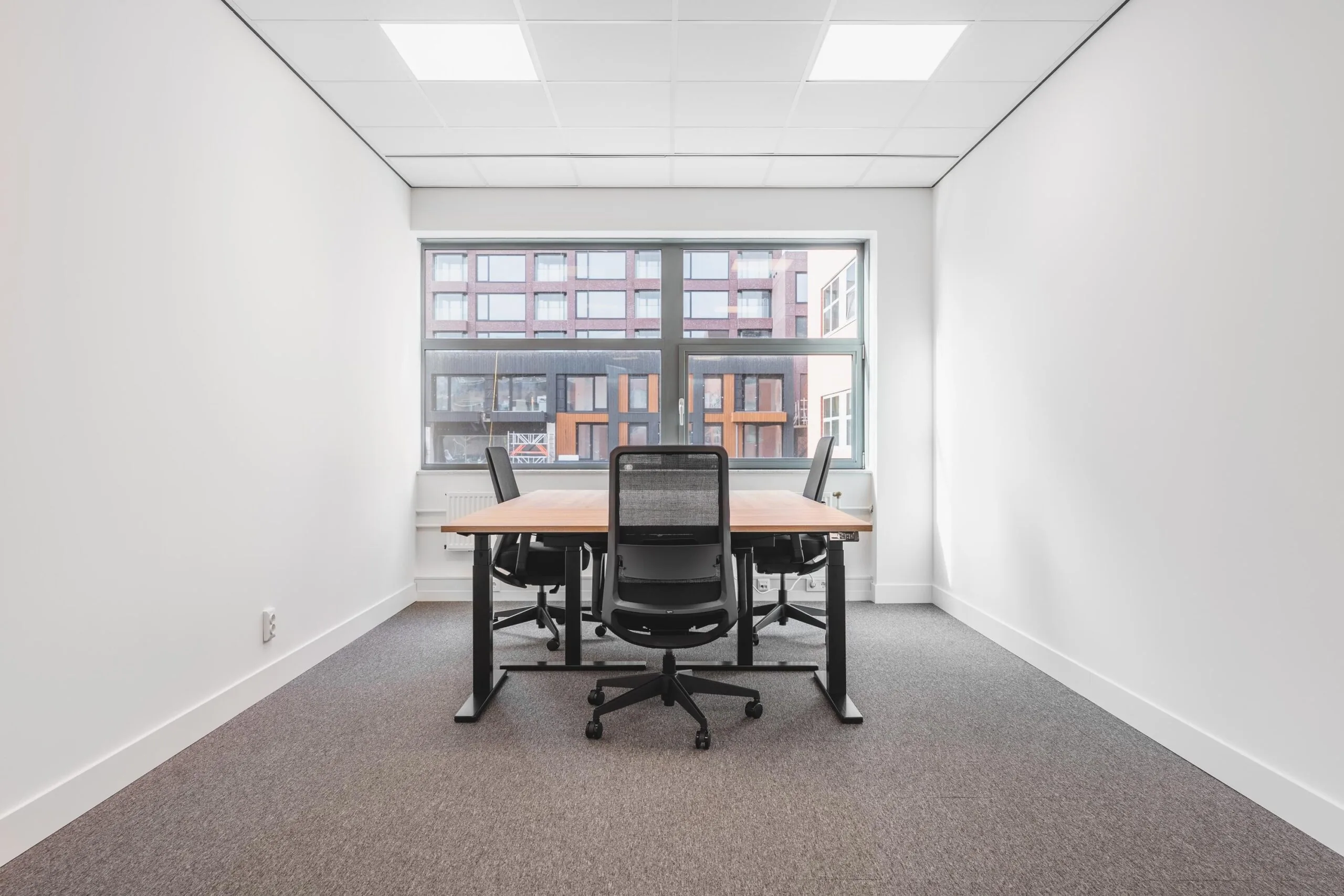 Modern, minimalistic office space with a wooden meeting table and four black chairs at Paasheuvelweg.
