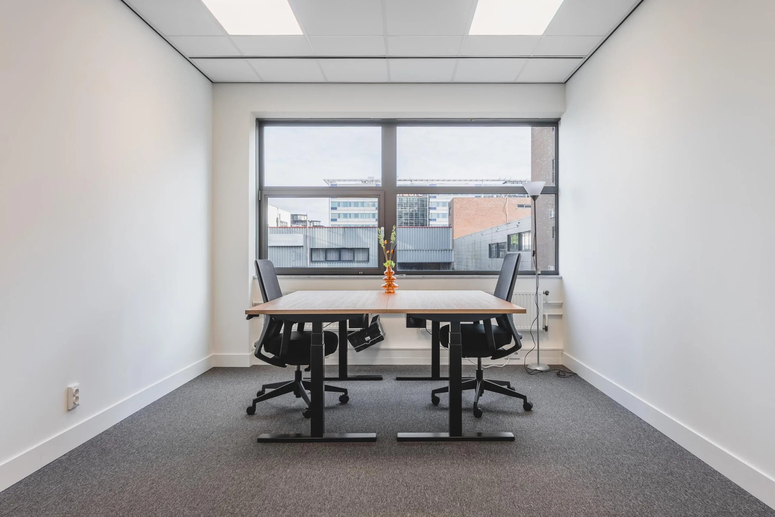 Modern office space at Paasheuvelweg with a wooden desk, two chairs, and a large window with a city view.