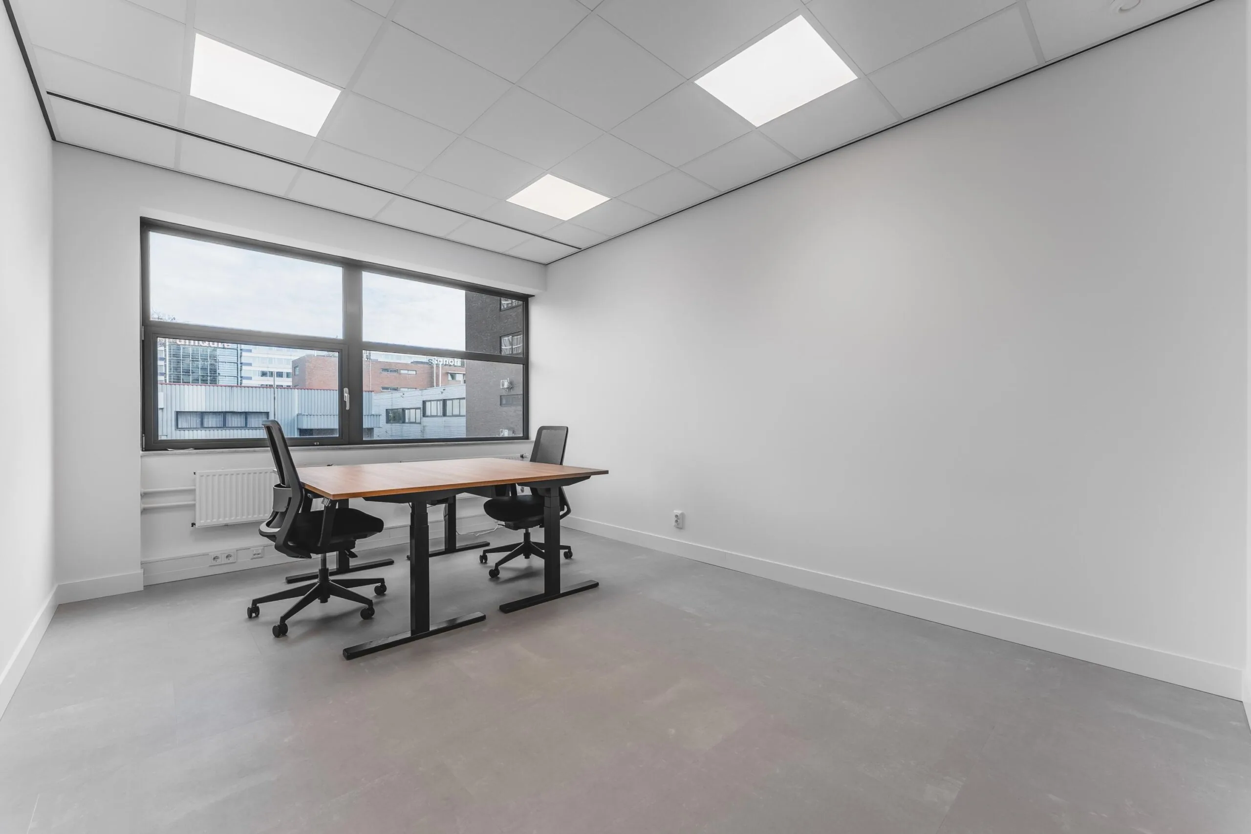 Modern, minimalistic office space at Paasheuvelweg with two chairs, a wooden desk, and a large window offering a view of nearby buildings.