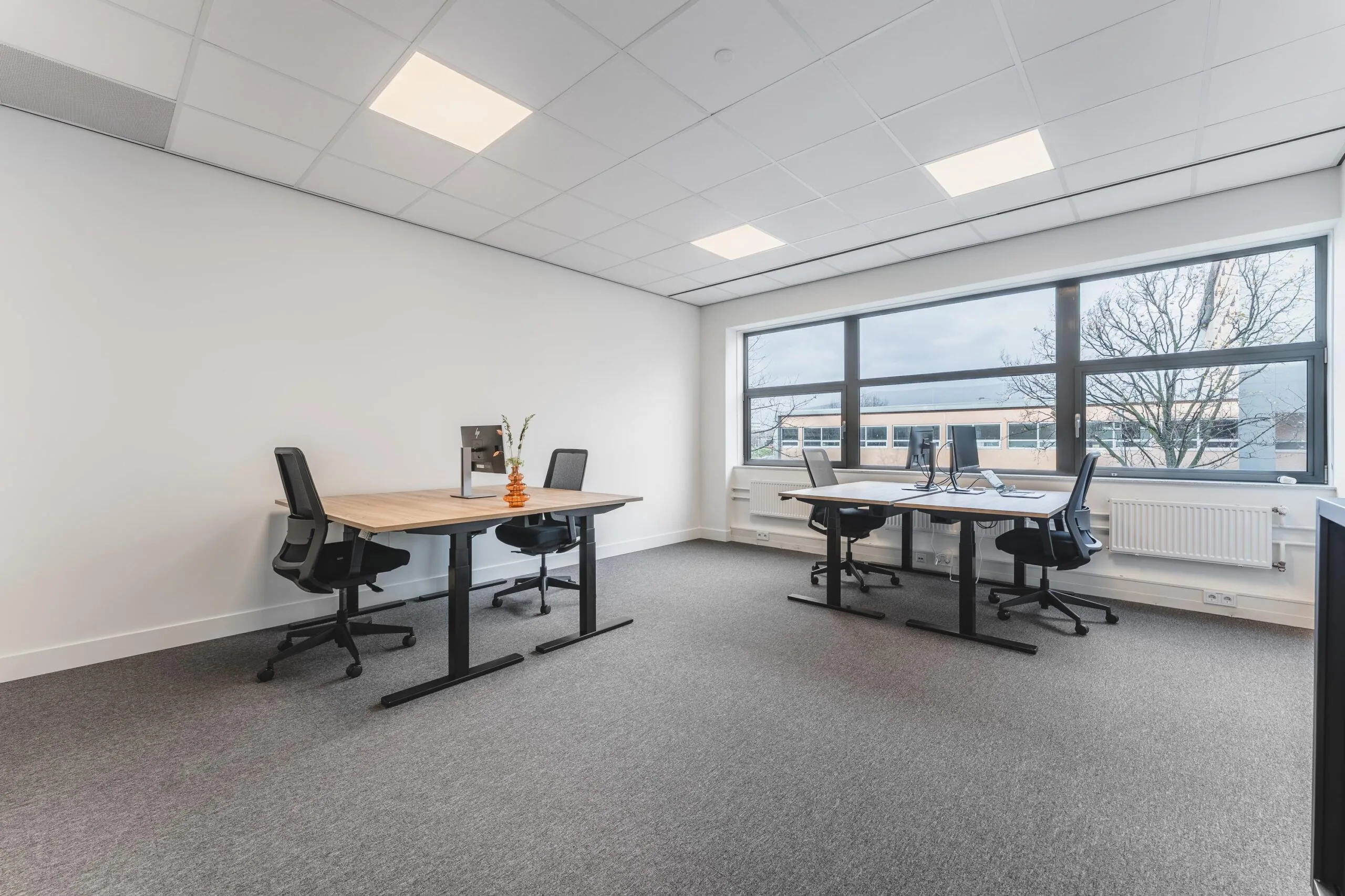 Modern office space on Paasheuvelweg with four workstations, large windows, and neutral decor.