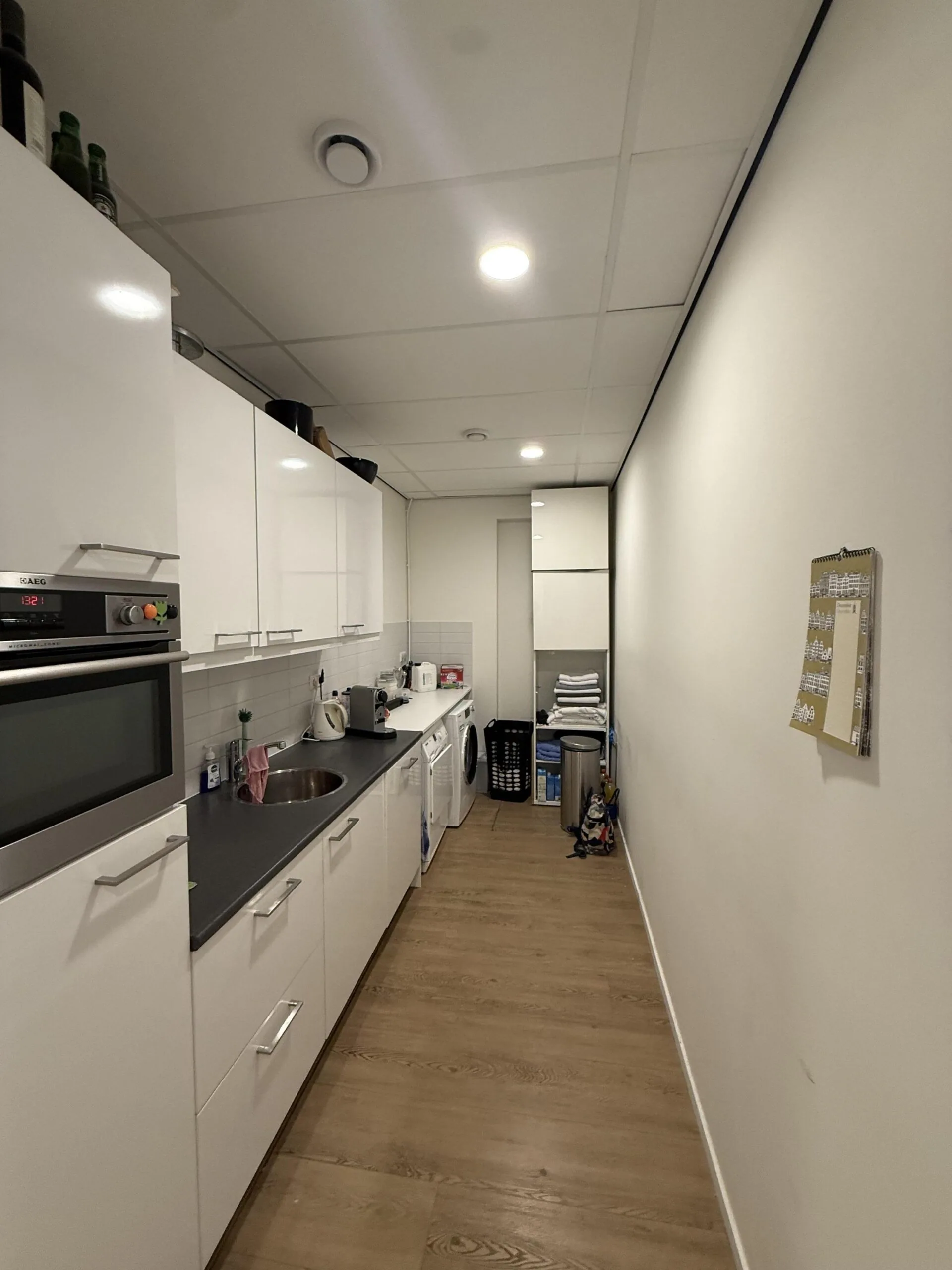 Modern galley kitchen with white cabinets, wooden flooring, and laundry appliances at the end of the room in a residence on Veteranenlaan.