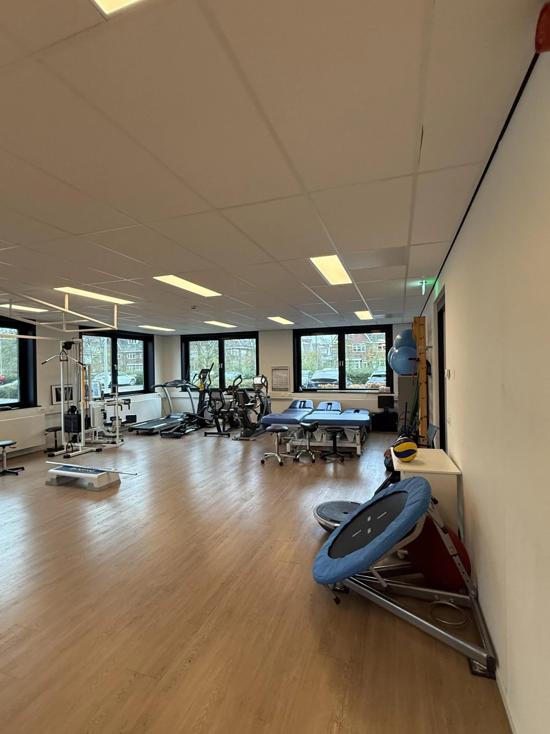 A spacious physiotherapy room on Veteranenlaan with exercise equipment, treatment tables, and large windows.