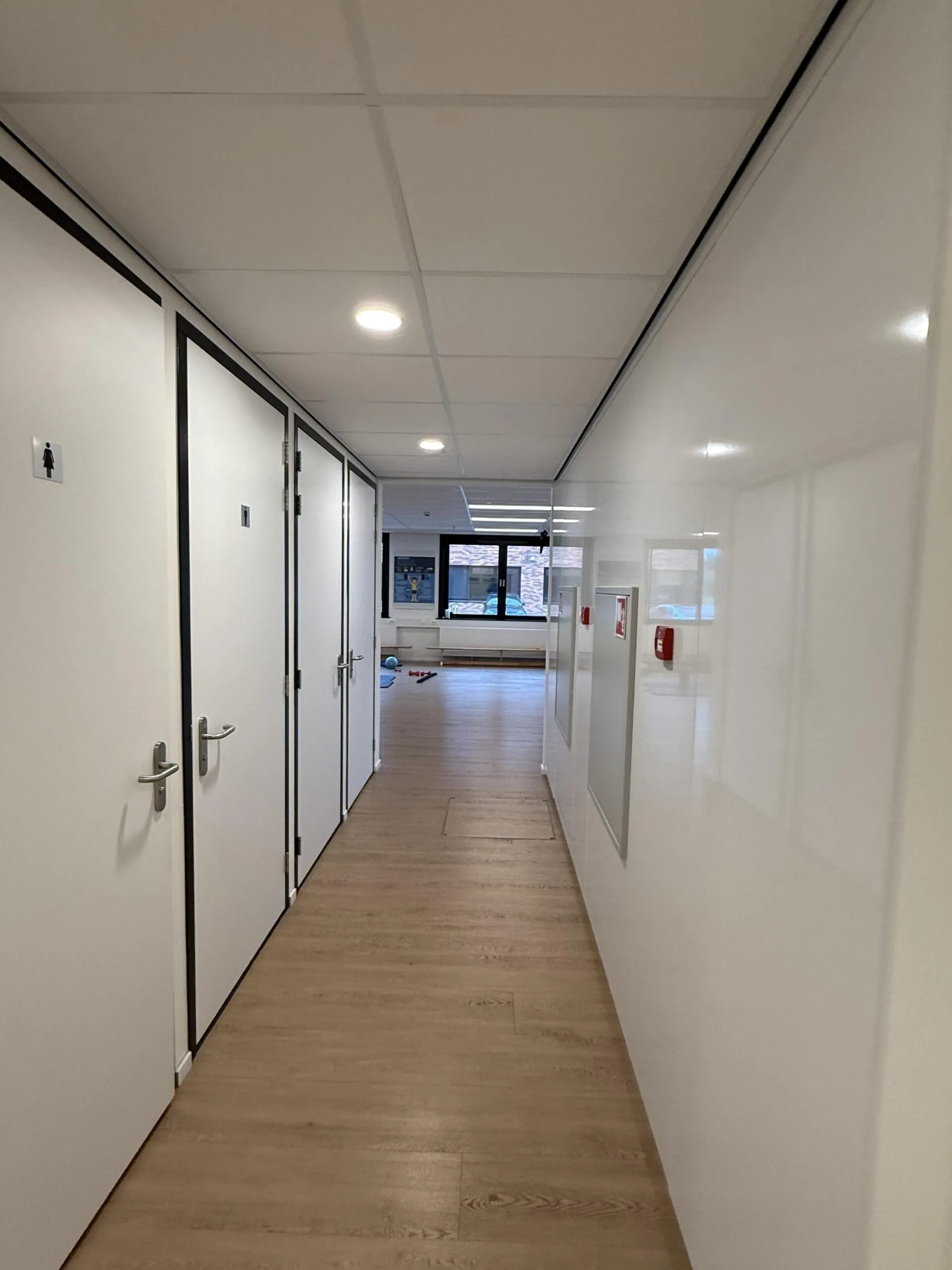 Hallway in the Veteranenlaan building with white doors, wooden flooring, and a window at the end letting in natural light.