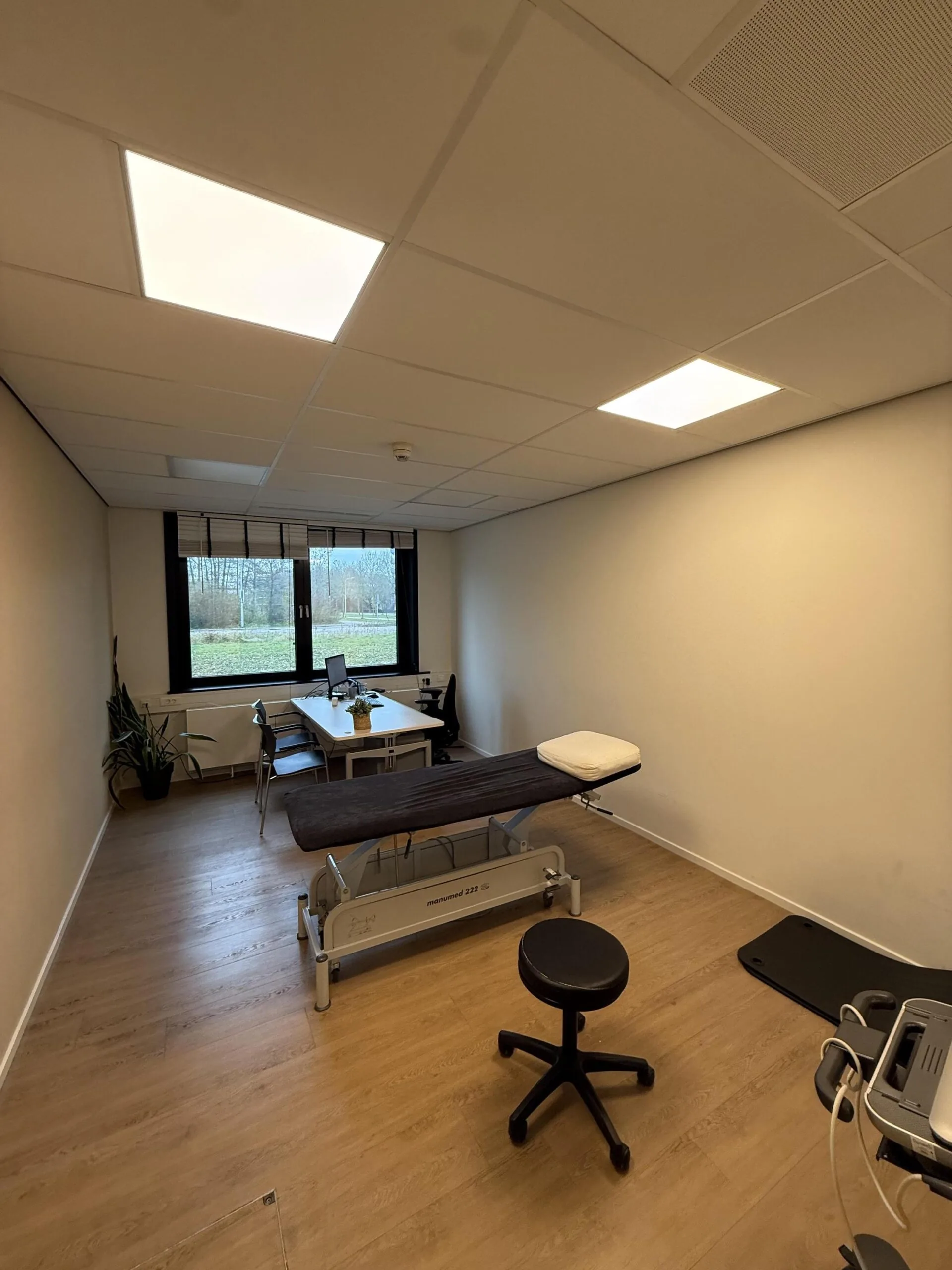 A modern medical consultation room on Veteranenlaan with a treatment table, desk, chairs, and medical equipment.