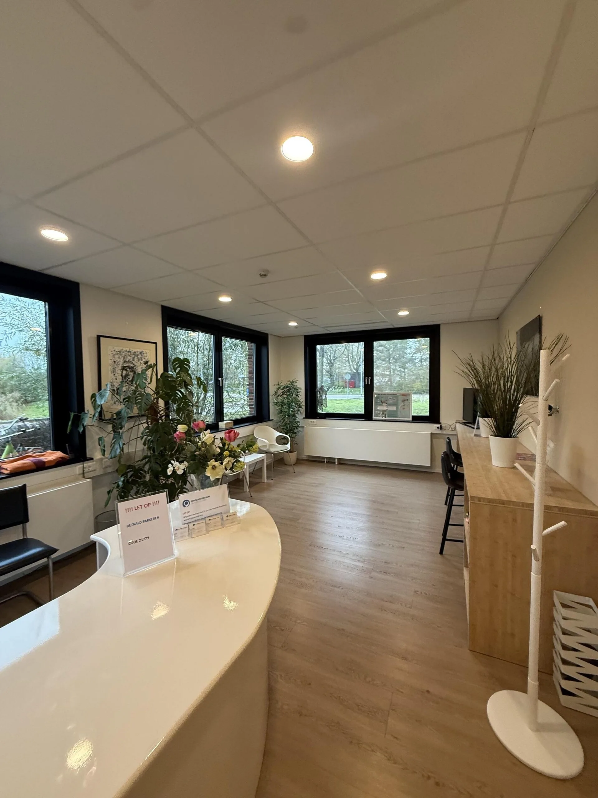Bright and modern waiting area at Veteranenlaan with a white reception desk, chairs, plants, and large windows.