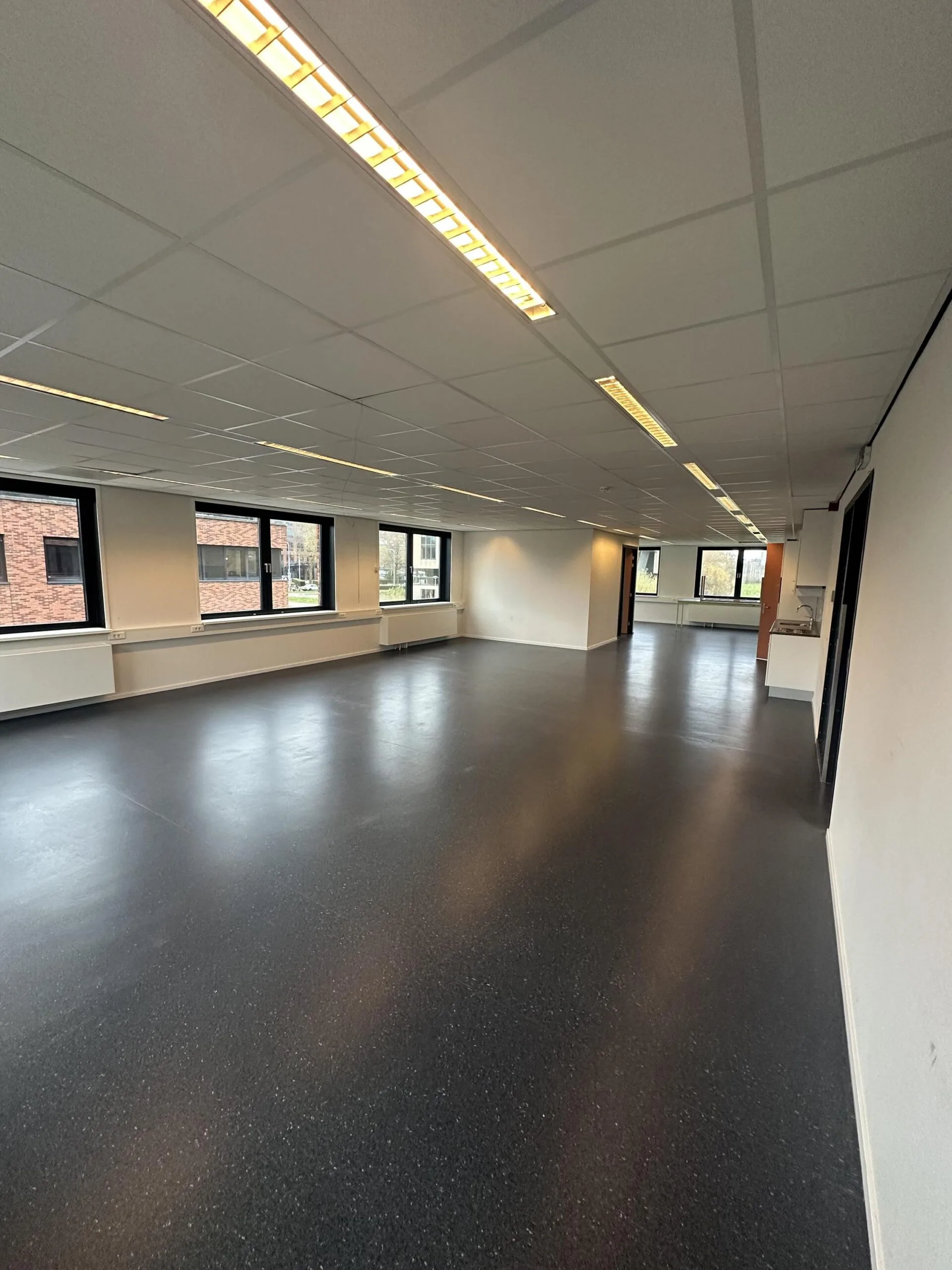 Empty office space with black flooring, white walls, and large windows on the Veteranenlaan.