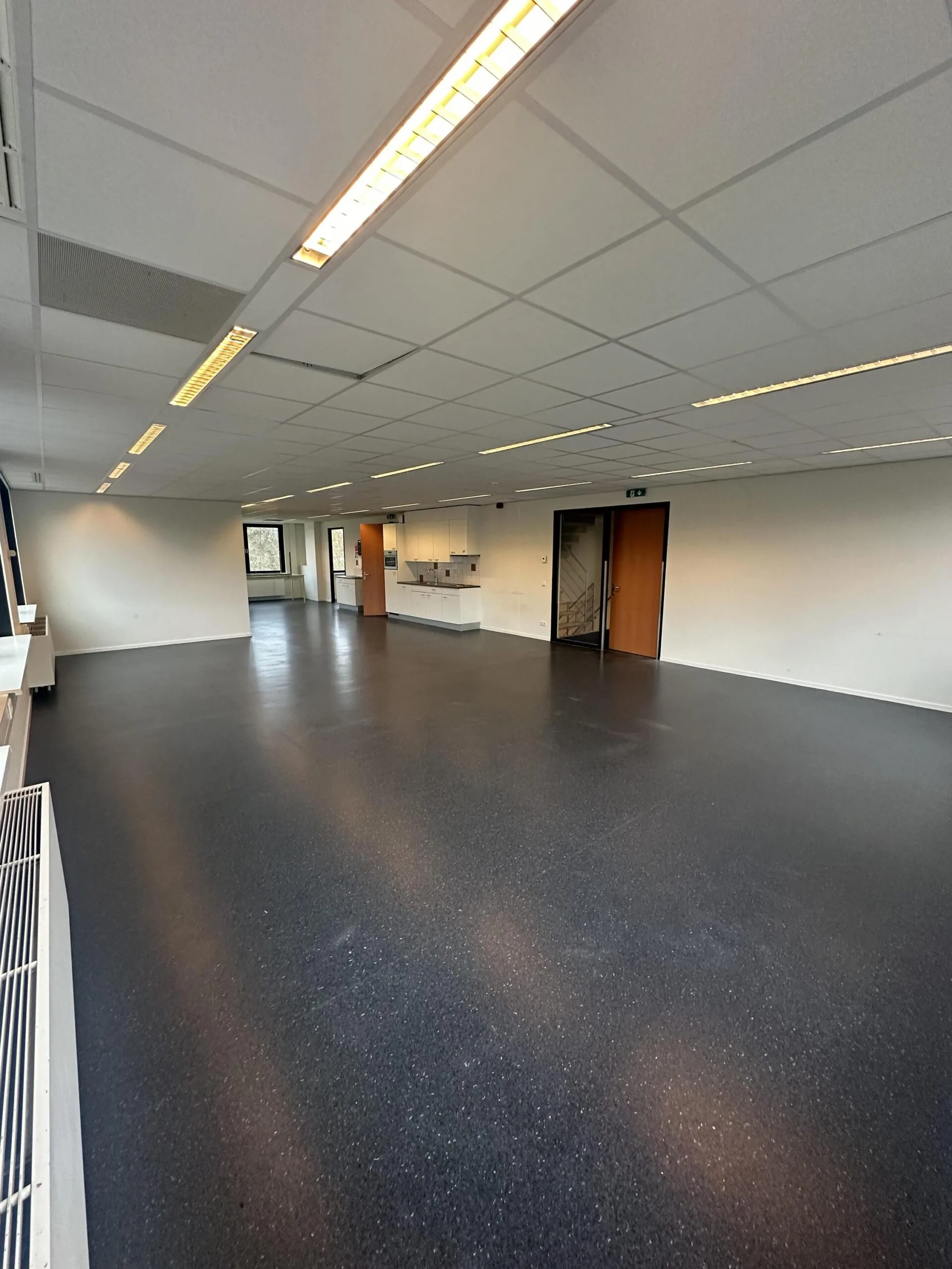Spacious, empty office interior on Veteranenlaan with dark flooring, white ceiling tiles, and built-in kitchenette.
