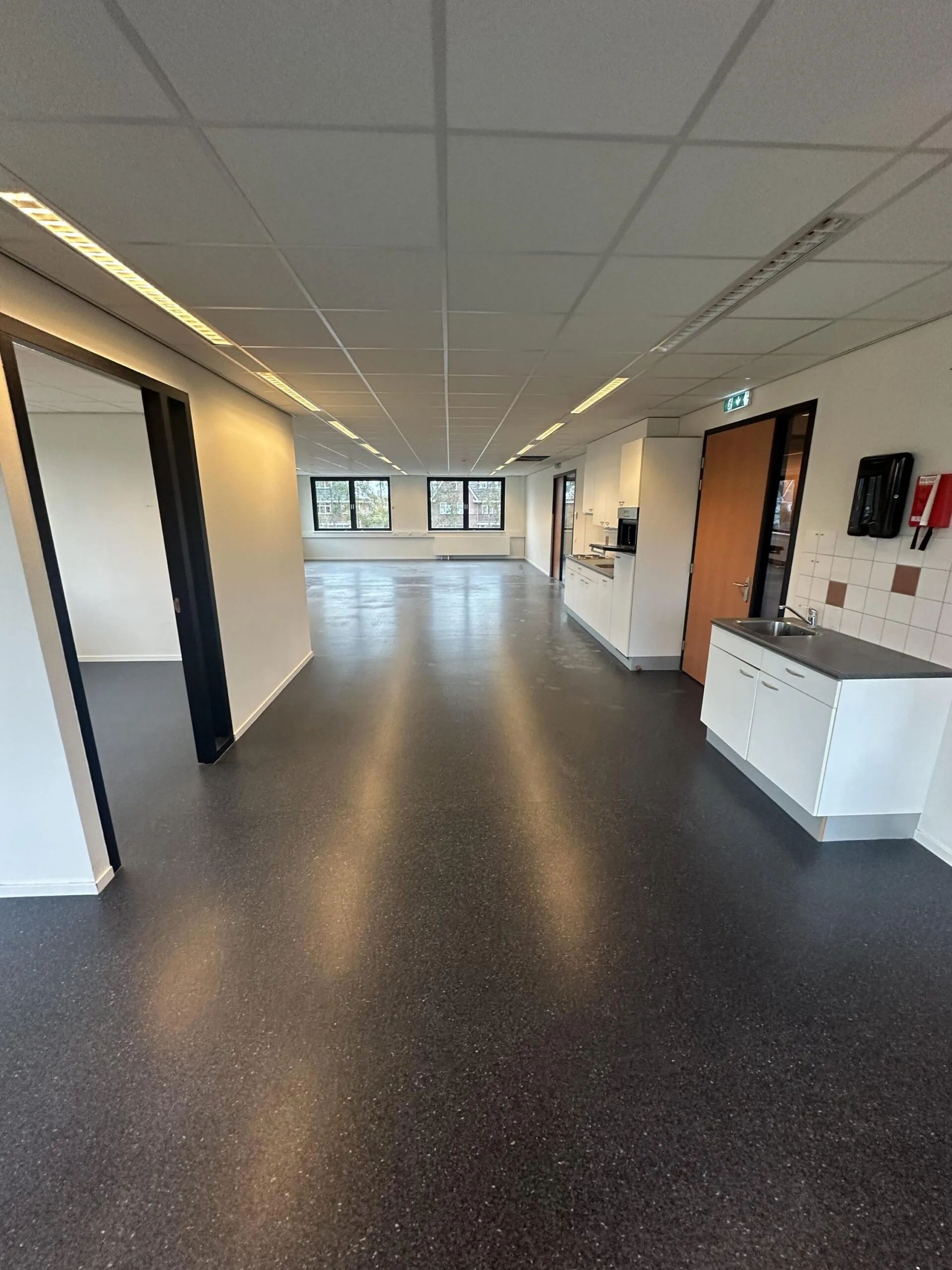 Bright office space on Veteranenlaan with a kitchenette, black flooring, and large windows.
