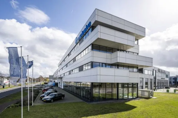 Modern office building of Exclusiva on Dynamostraat with parked cars and waving flags in front.