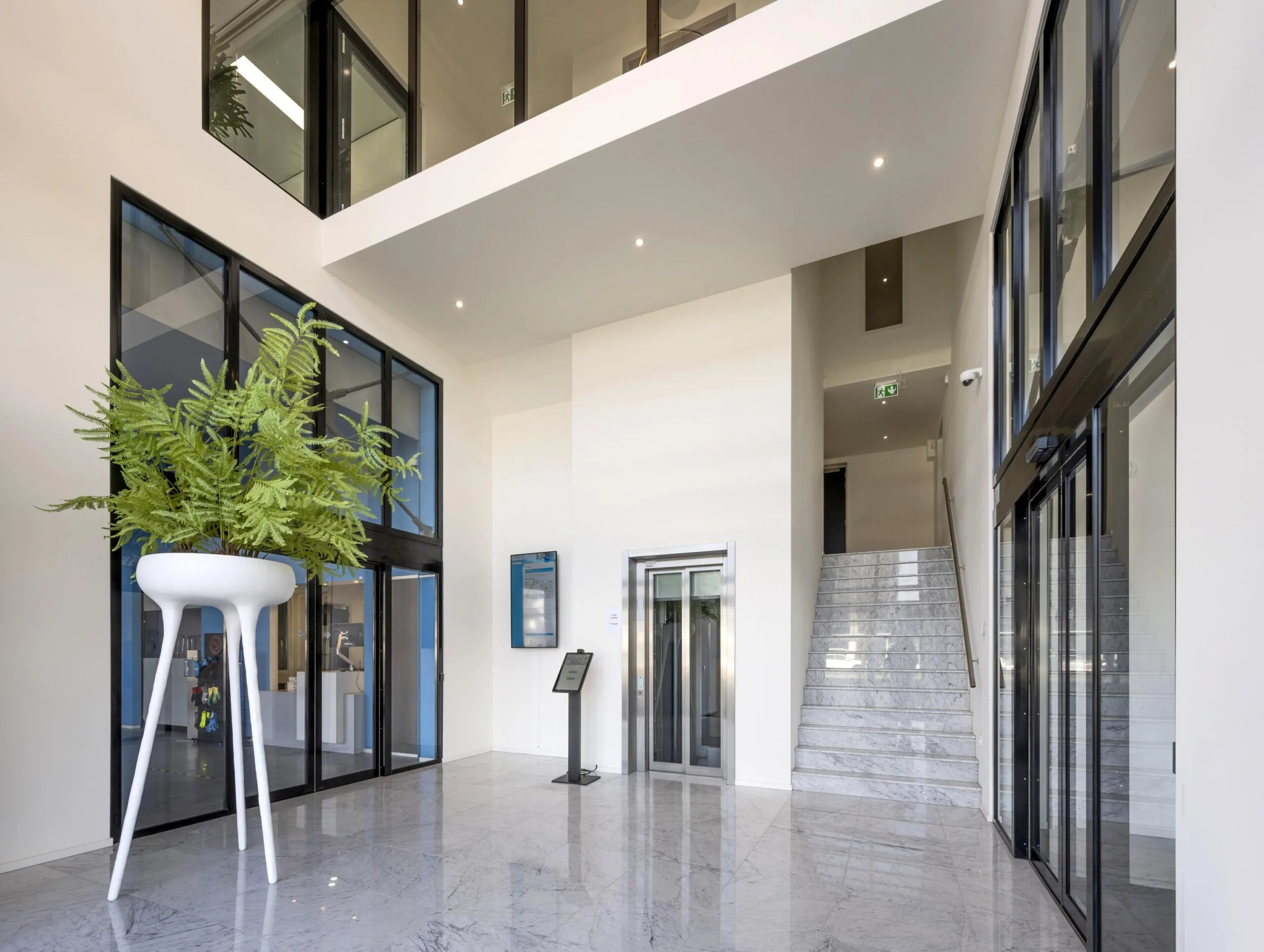 Modern lobby interior at Dynamostraat with marble flooring, a large white planter, glass walls, elevator, and staircase.
