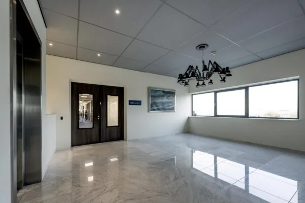 Modern office hallway at Dynamostraat with marble flooring, large windows, and a distinctive black chandelier.