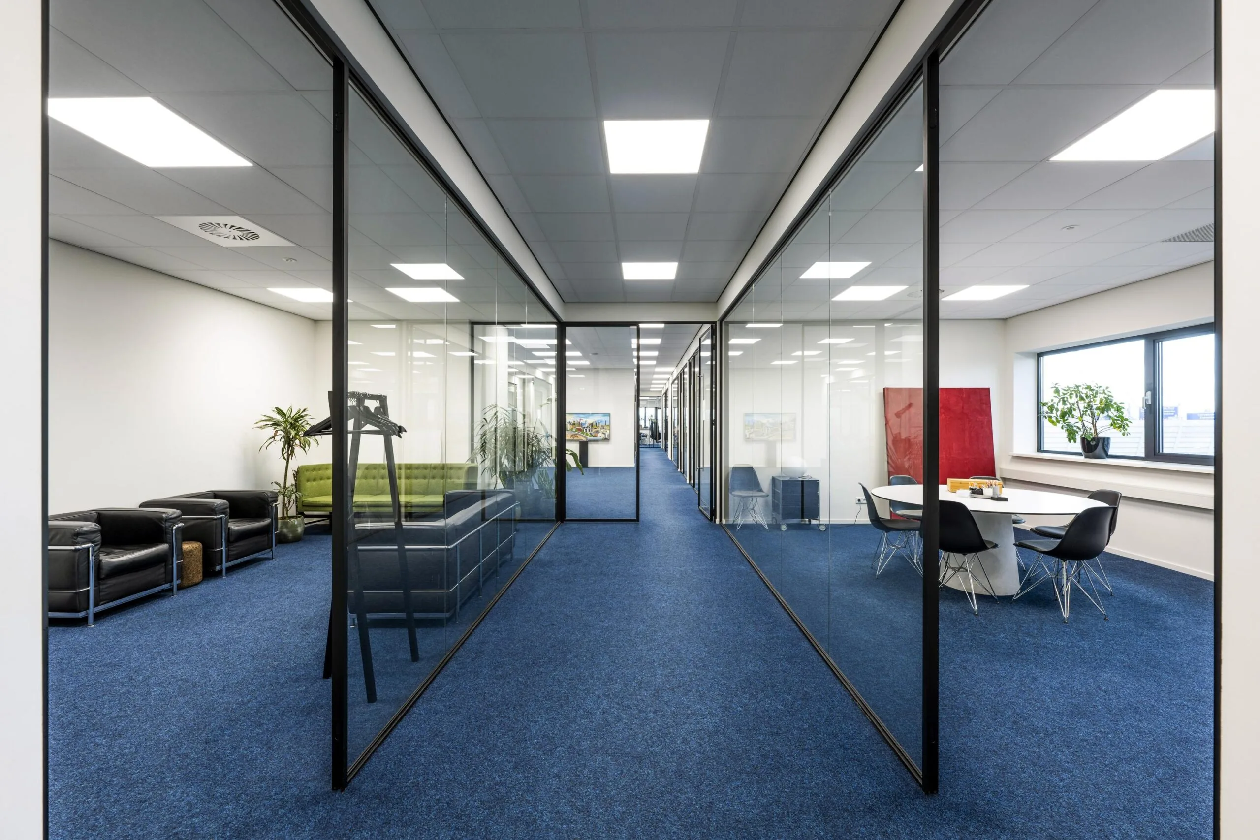 Modern office hallway at Dynamostraat with glass walls, blue carpet, and contemporary furnishings.