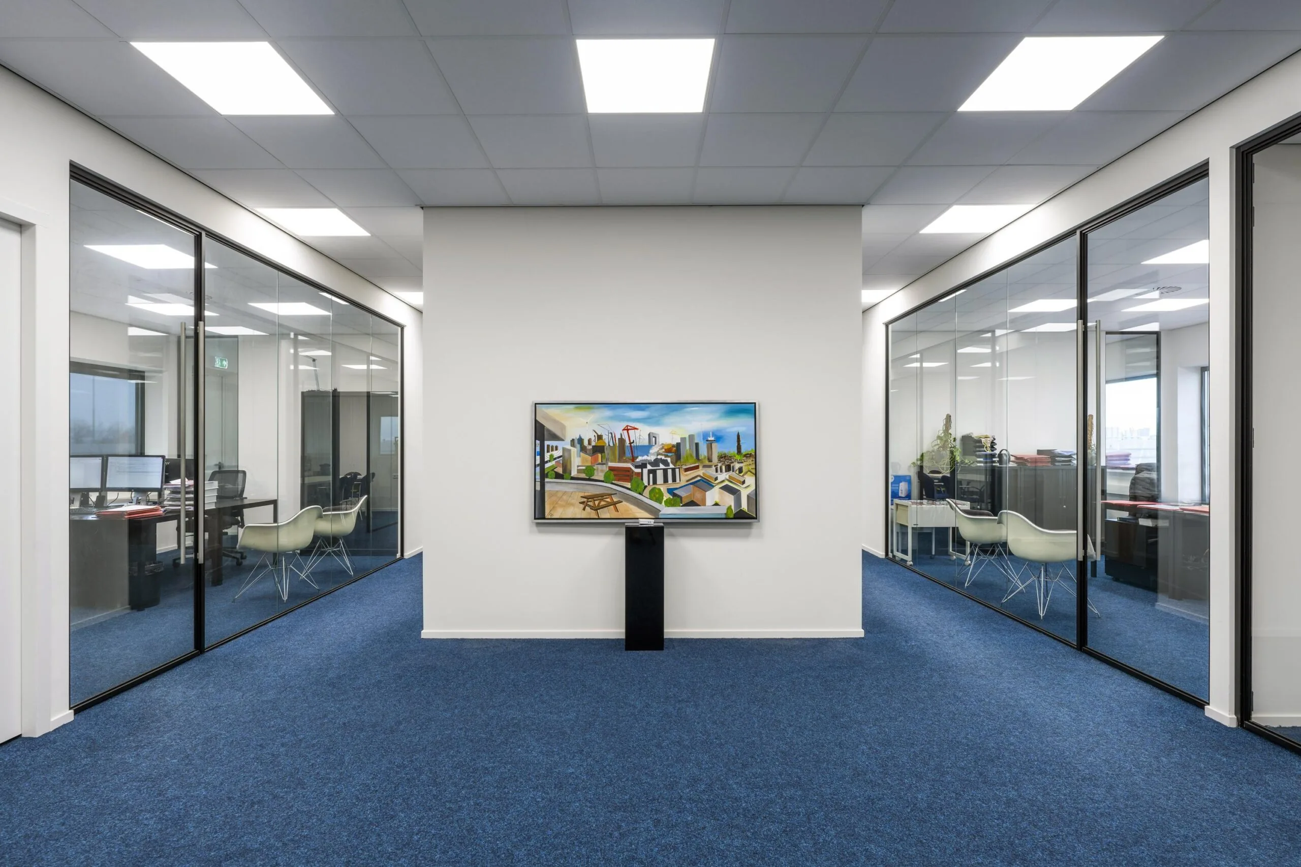 Modern office hallway with blue carpet, glass-walled meeting rooms, and a colorful cityscape painting on the end wall at Dynamostraat.
