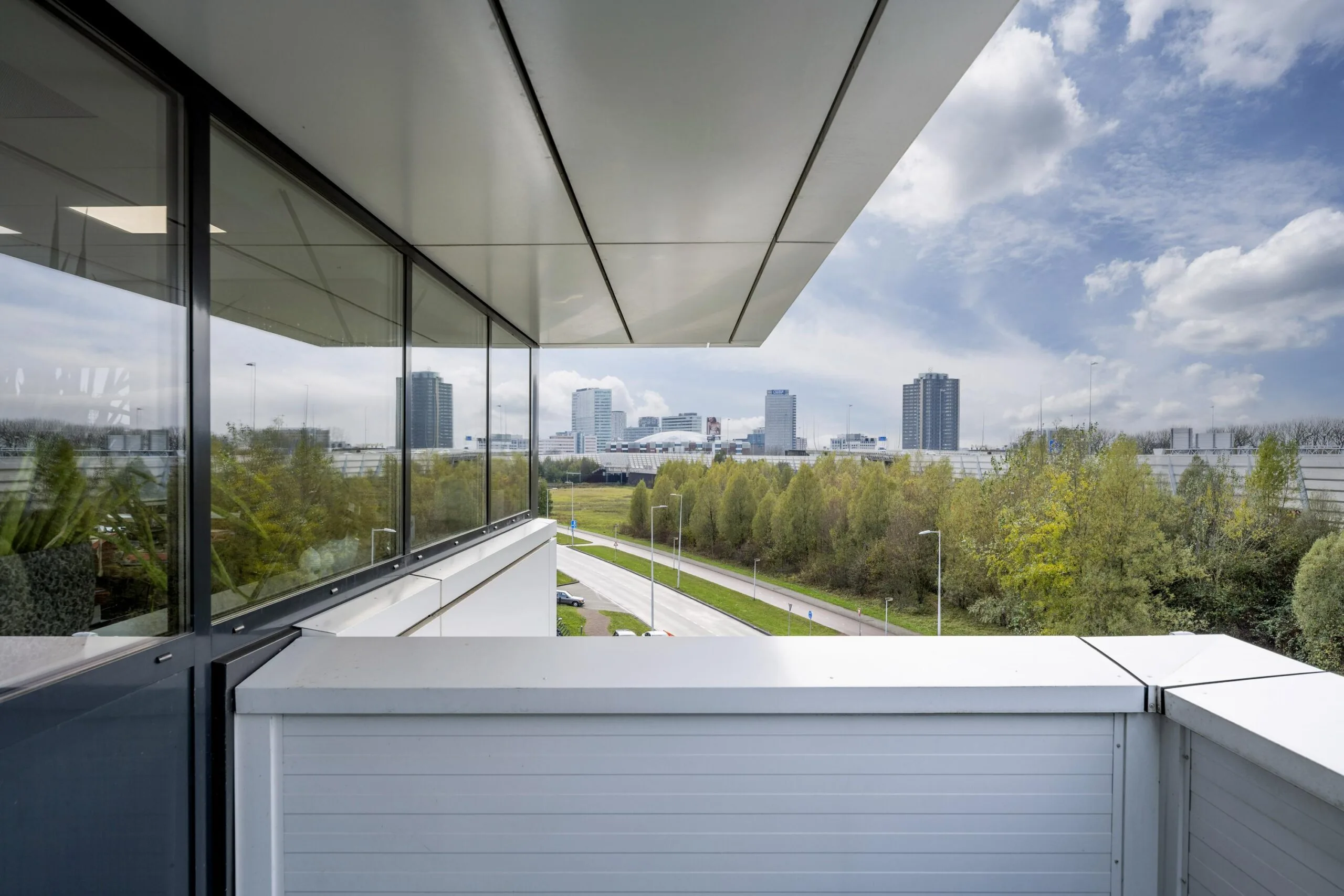 View from a balcony on Dynamostraat overlooking a tree-lined road and the city skyline with modern high-rise buildings.