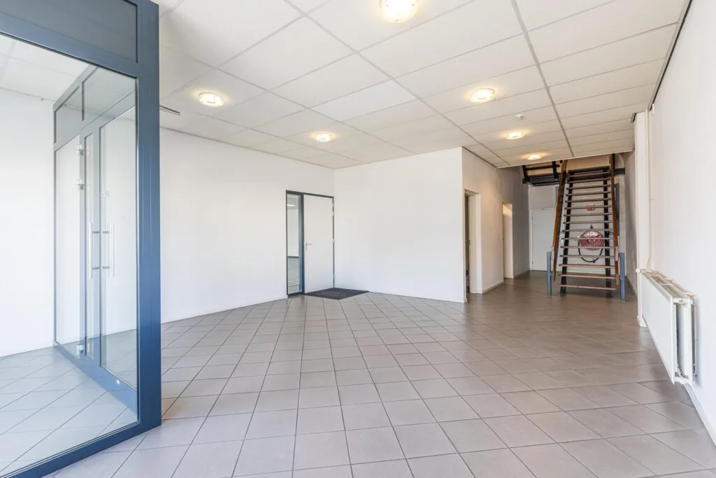 Spacious and bright commercial interior with tiled flooring, glass office partition, and wooden staircase at Zonnebaan.