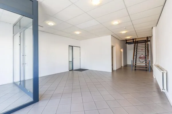 Spacious and bright commercial interior with tiled flooring, glass office partition, and wooden staircase at Zonnebaan.