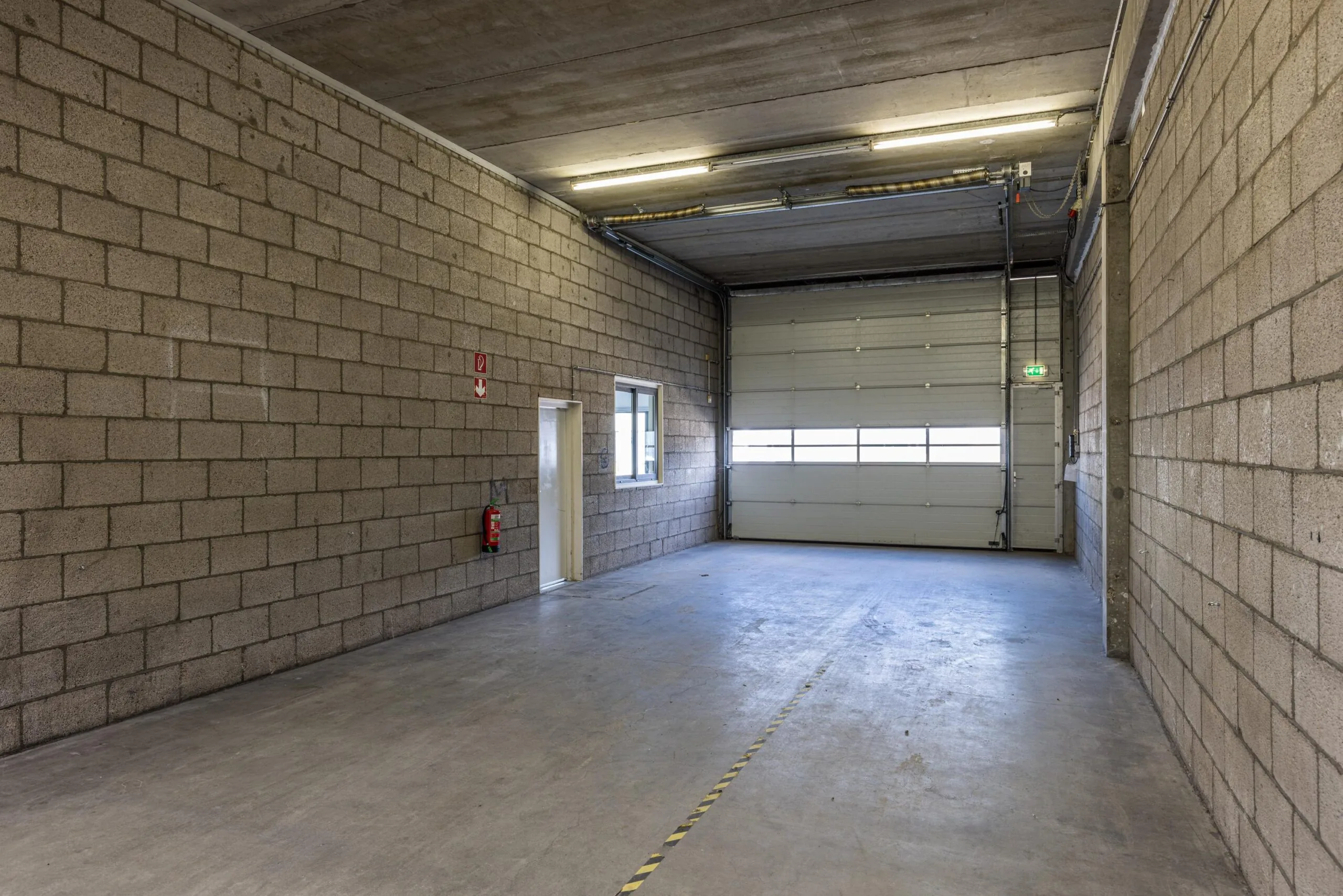 Empty industrial warehouse unit with concrete walls, a large rolling door, and fluorescent ceiling lights on Zonnebaan.