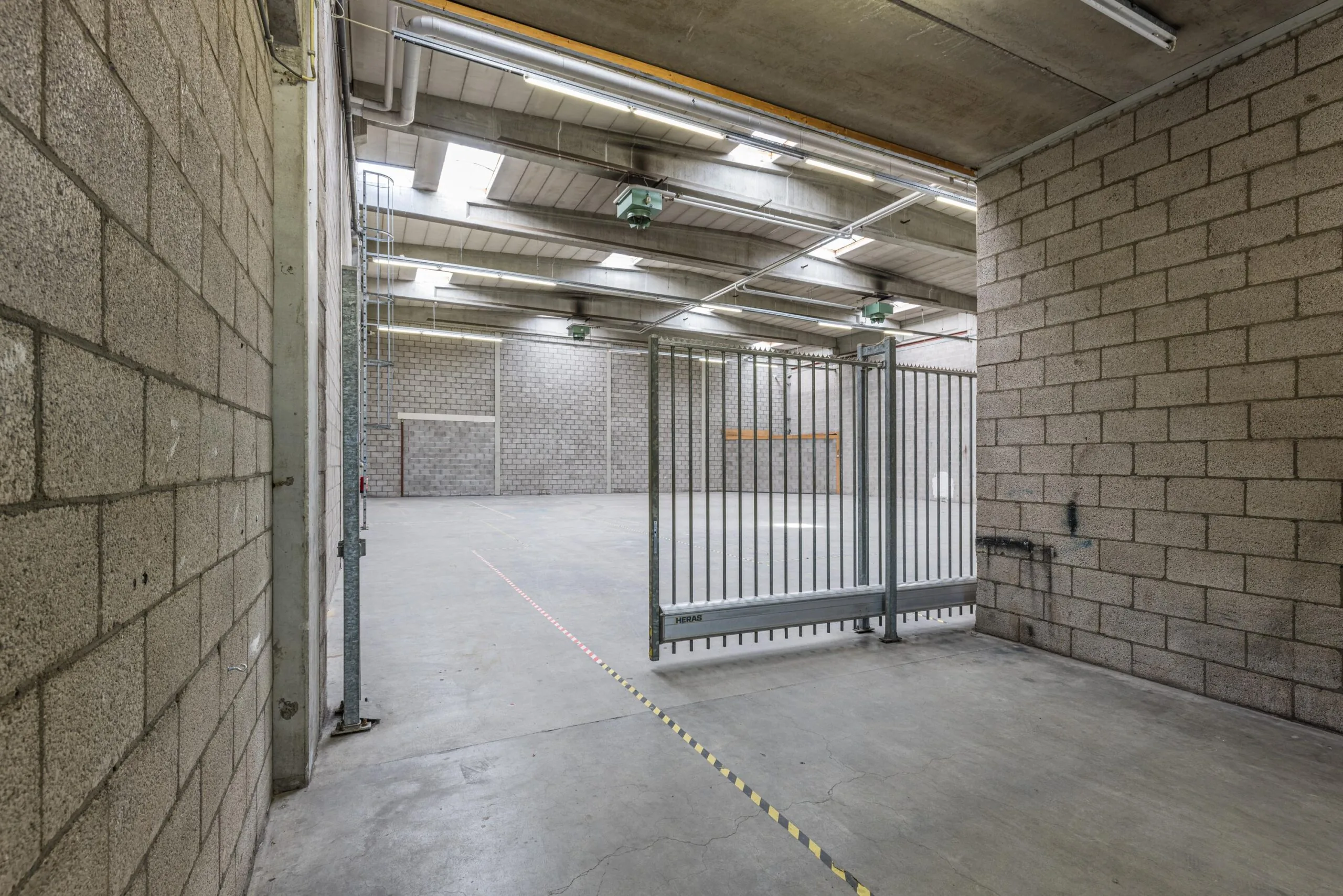 Large empty industrial warehouse with concrete walls, skylights, and a metal gate at Zonnebaan.