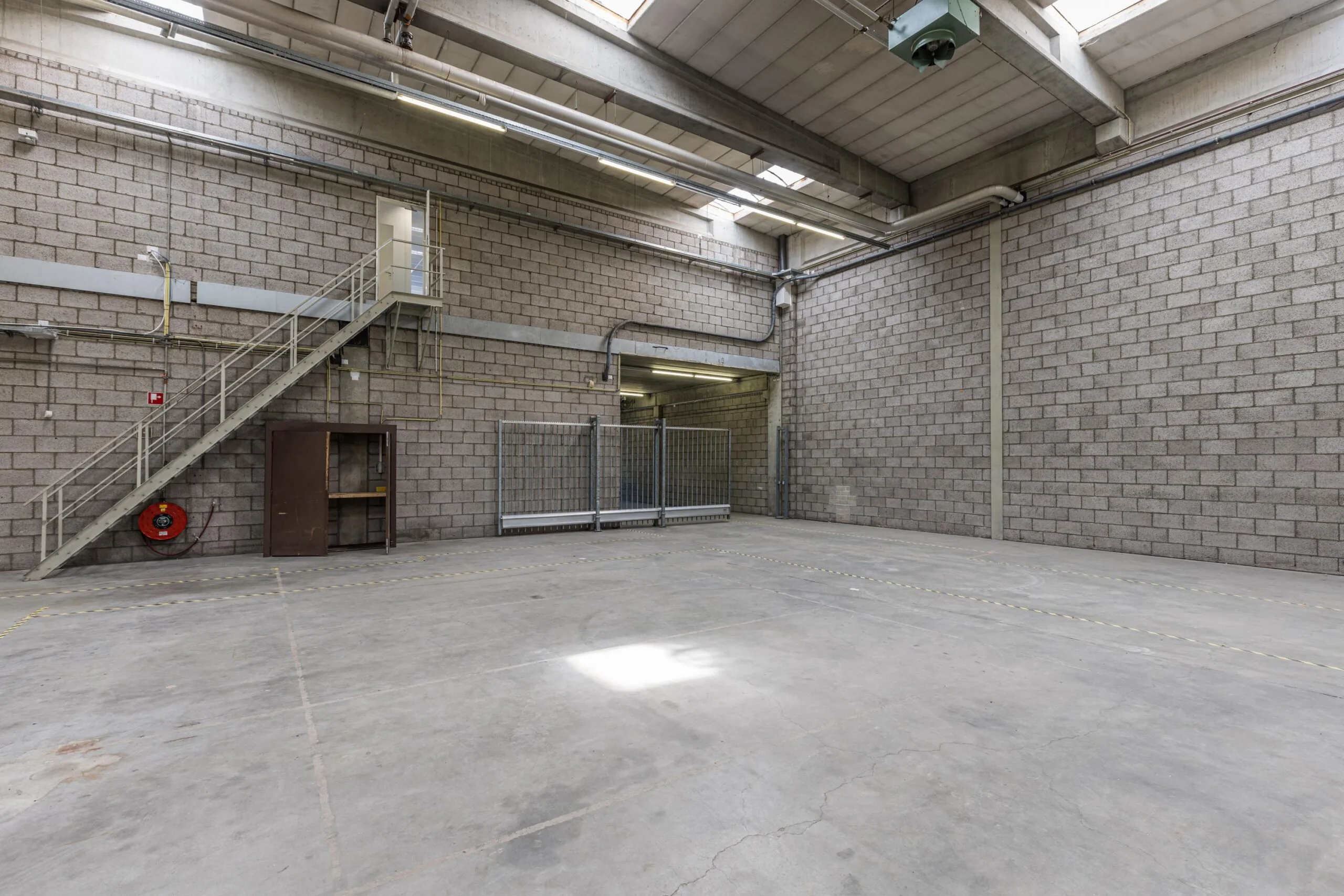 Empty industrial warehouse unit with high ceilings, concrete floor, staircase, and a metal gate, located at Zonnebaan.
