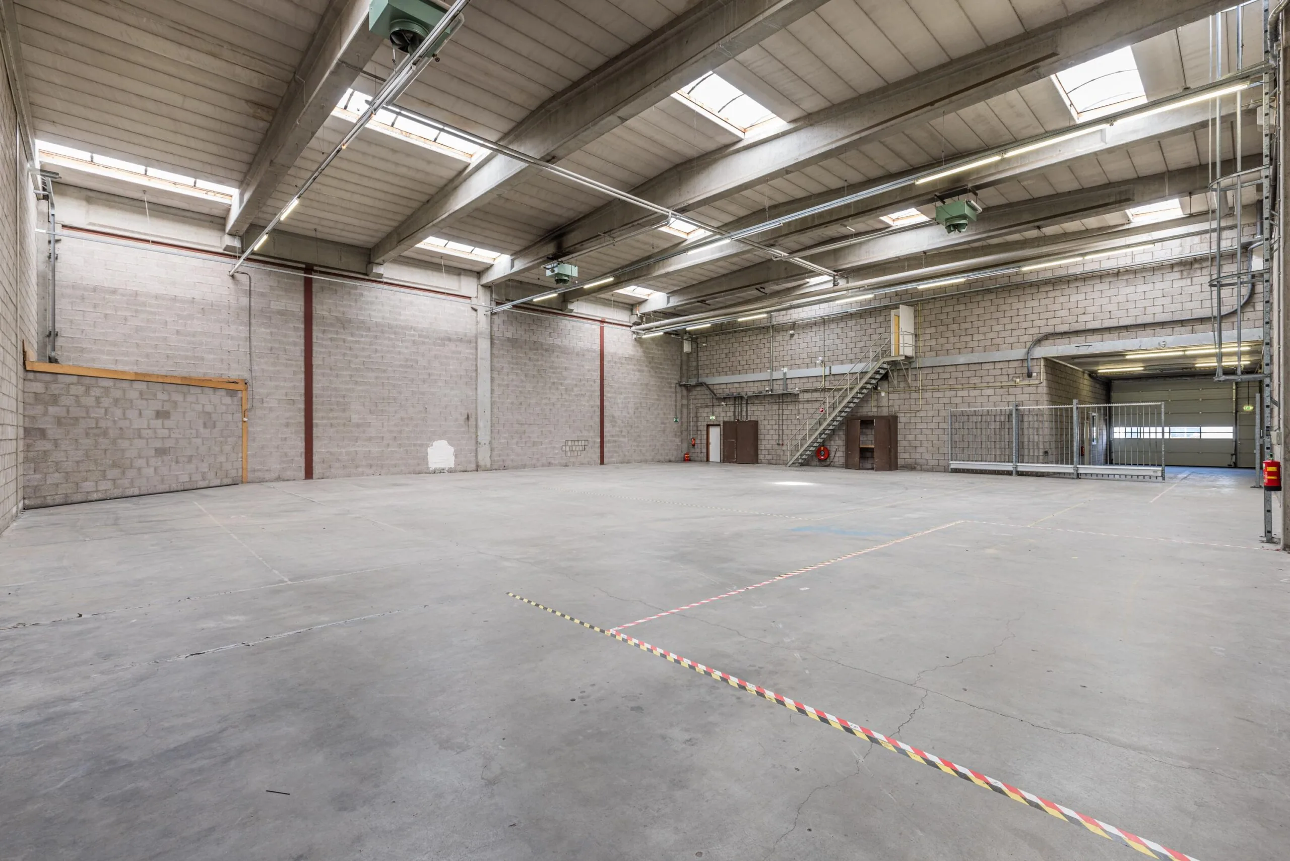 Spacious industrial warehouse with concrete flooring, skylights, and a metal staircase near Zonnebaan 176 in Utrecht.