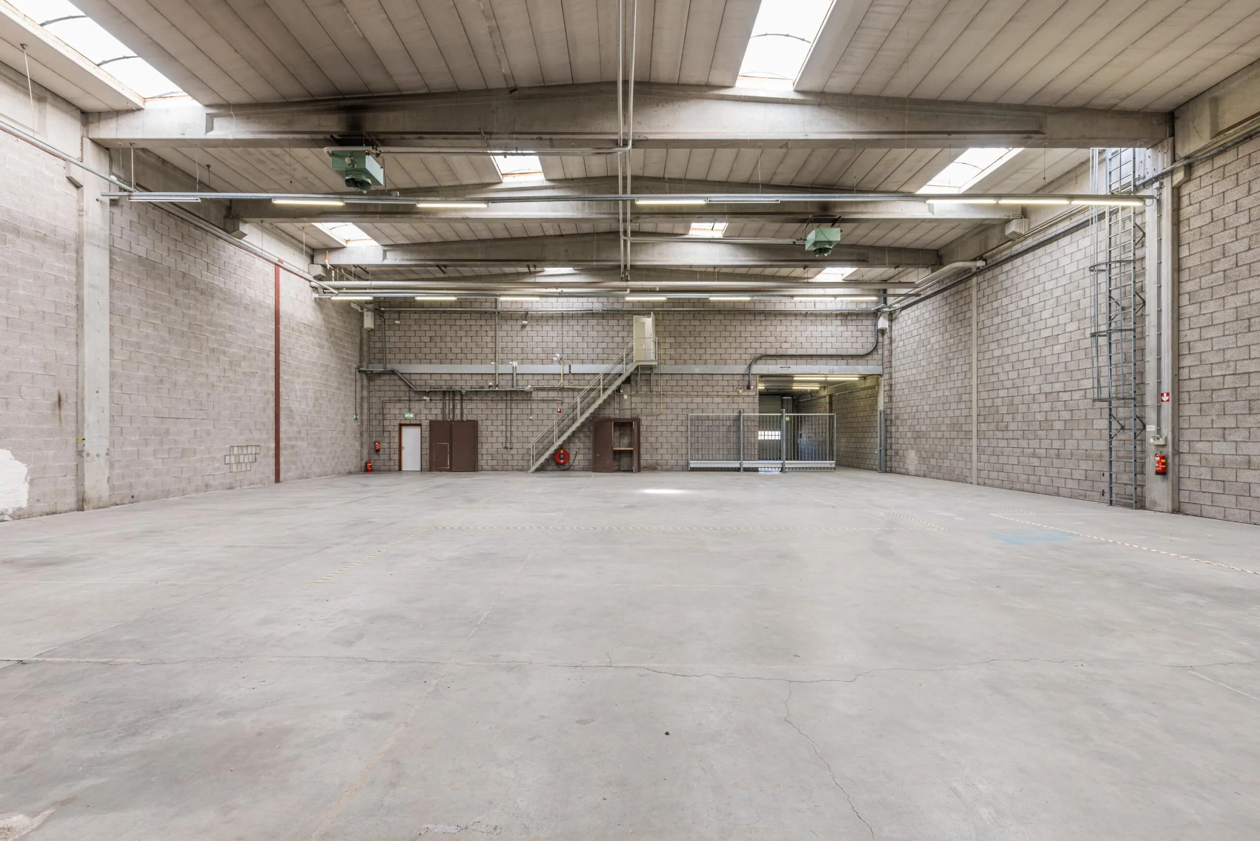 Spacious and empty industrial warehouse on Zonnebaan with concrete floors, brick walls, and skylights.