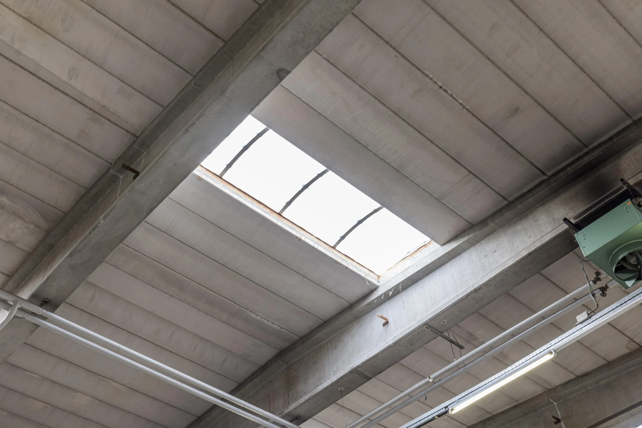 Industrial ceiling with a skylight at Zonnebaan, showing structural beams, pipes, and ventilation system.