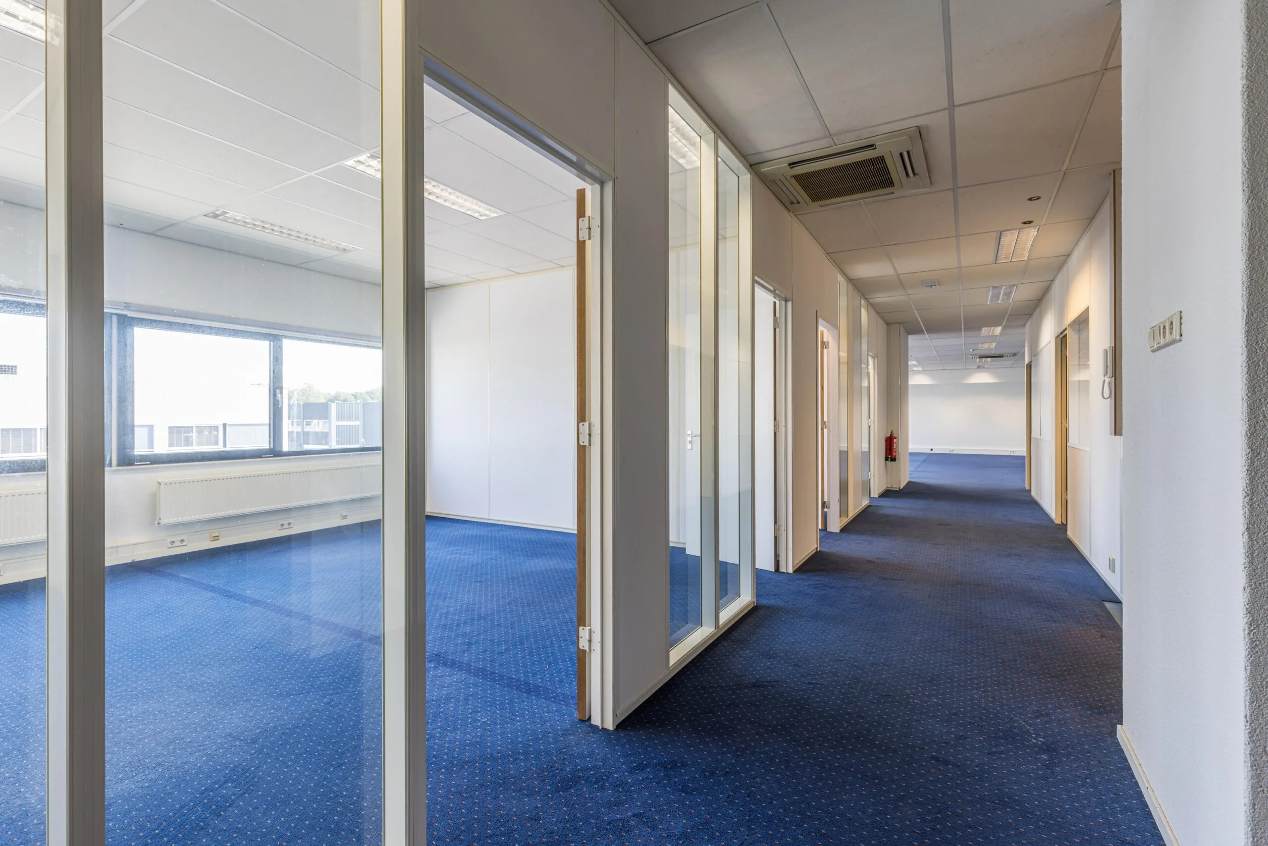 Office hallway with glass-walled rooms and blue carpet at Zonnebaan 20 in Utrecht.
