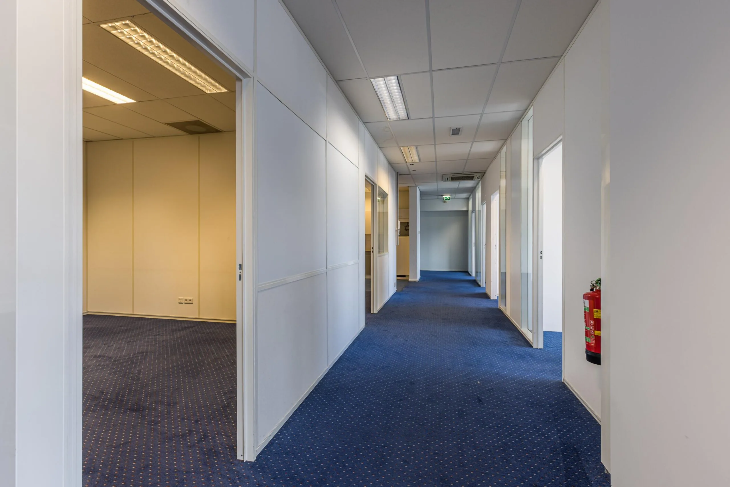 Office hallway at Zonnebaan with blue carpet, white walls, and several open doors to empty rooms.