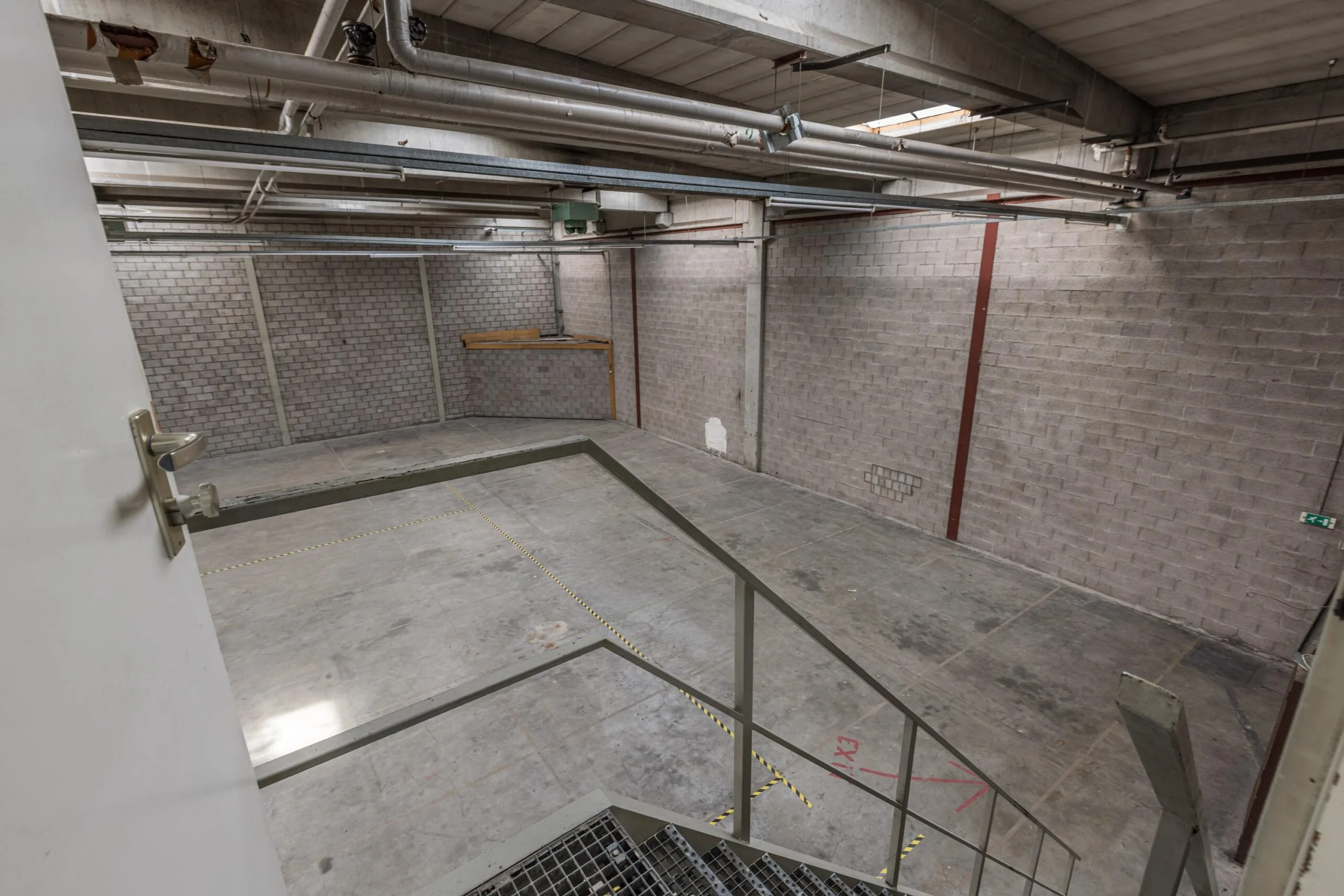 Empty industrial warehouse space with concrete floors and brick walls viewed from a staircase.