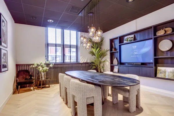Modern meeting room on Lage Naarderweg with a black oval table, textured chairs, pendant lighting, and a built-in screen.